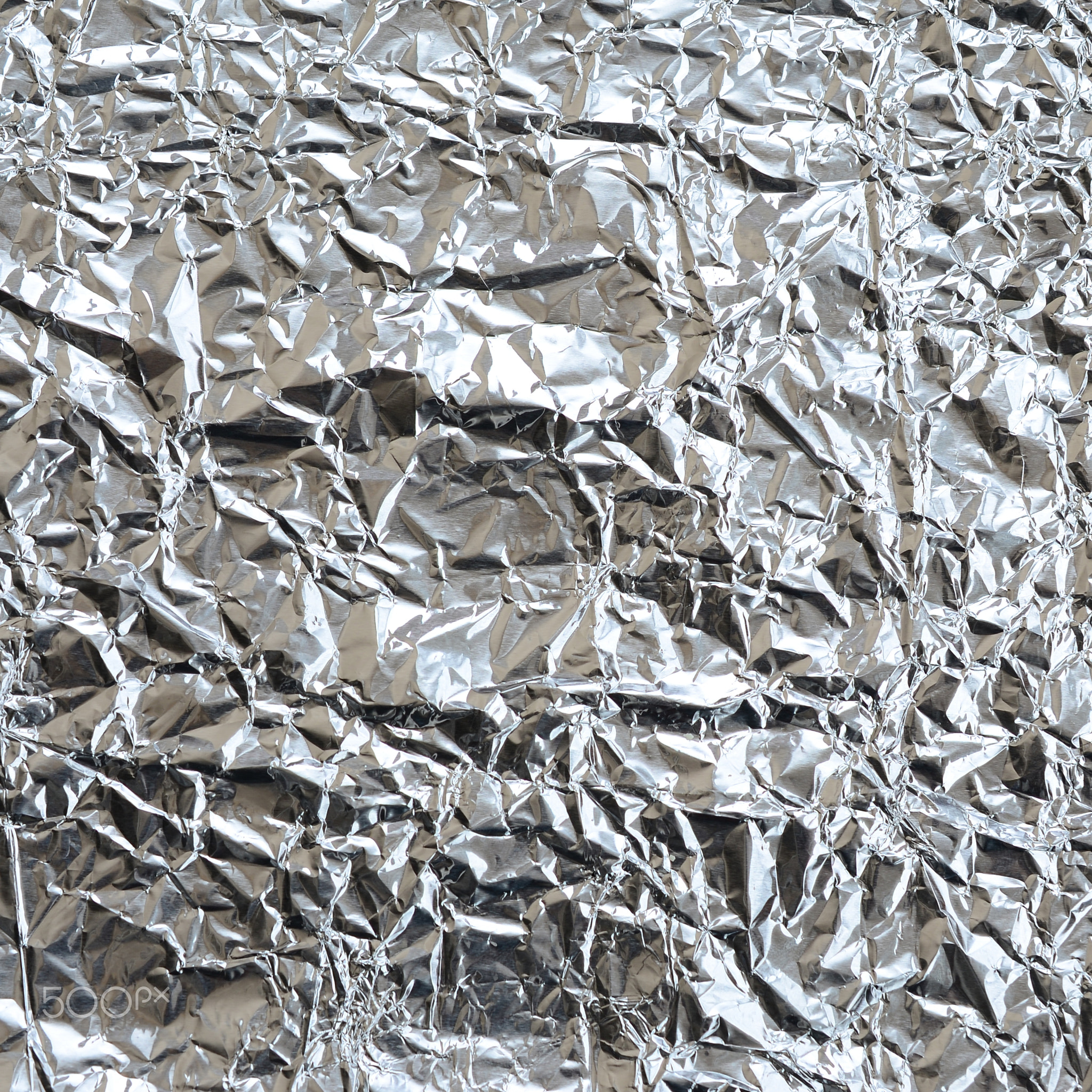 Thin wrinkled sheet of crushed tin aluminum silver foil background with shiny crumpled surface for