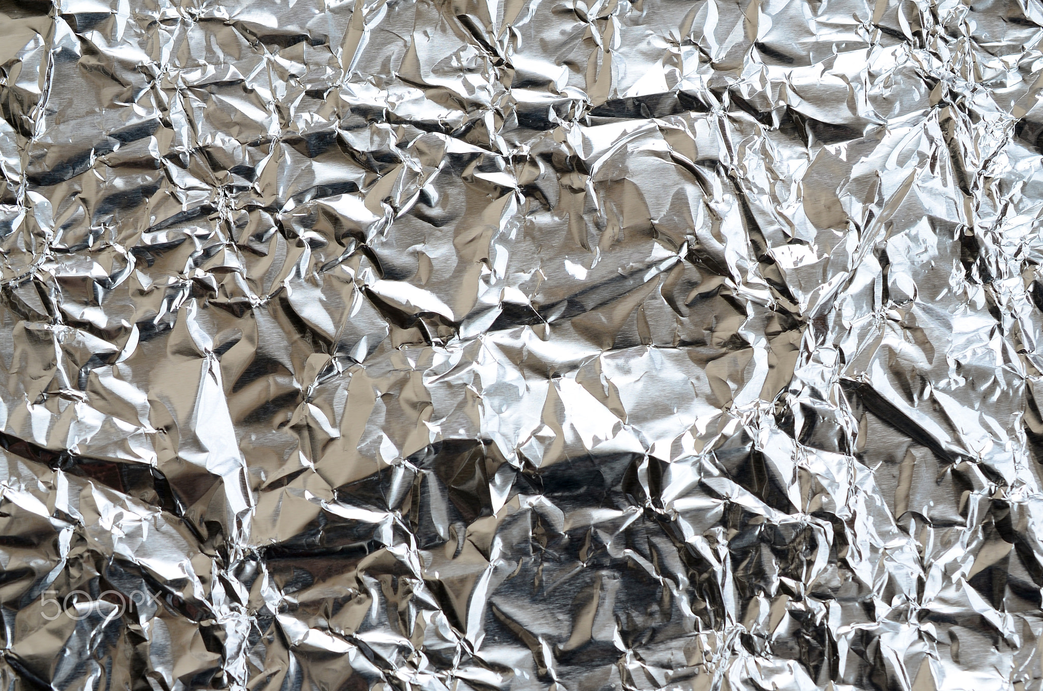 Thin wrinkled sheet of crushed tin aluminum silver foil background with shiny crumpled surface for