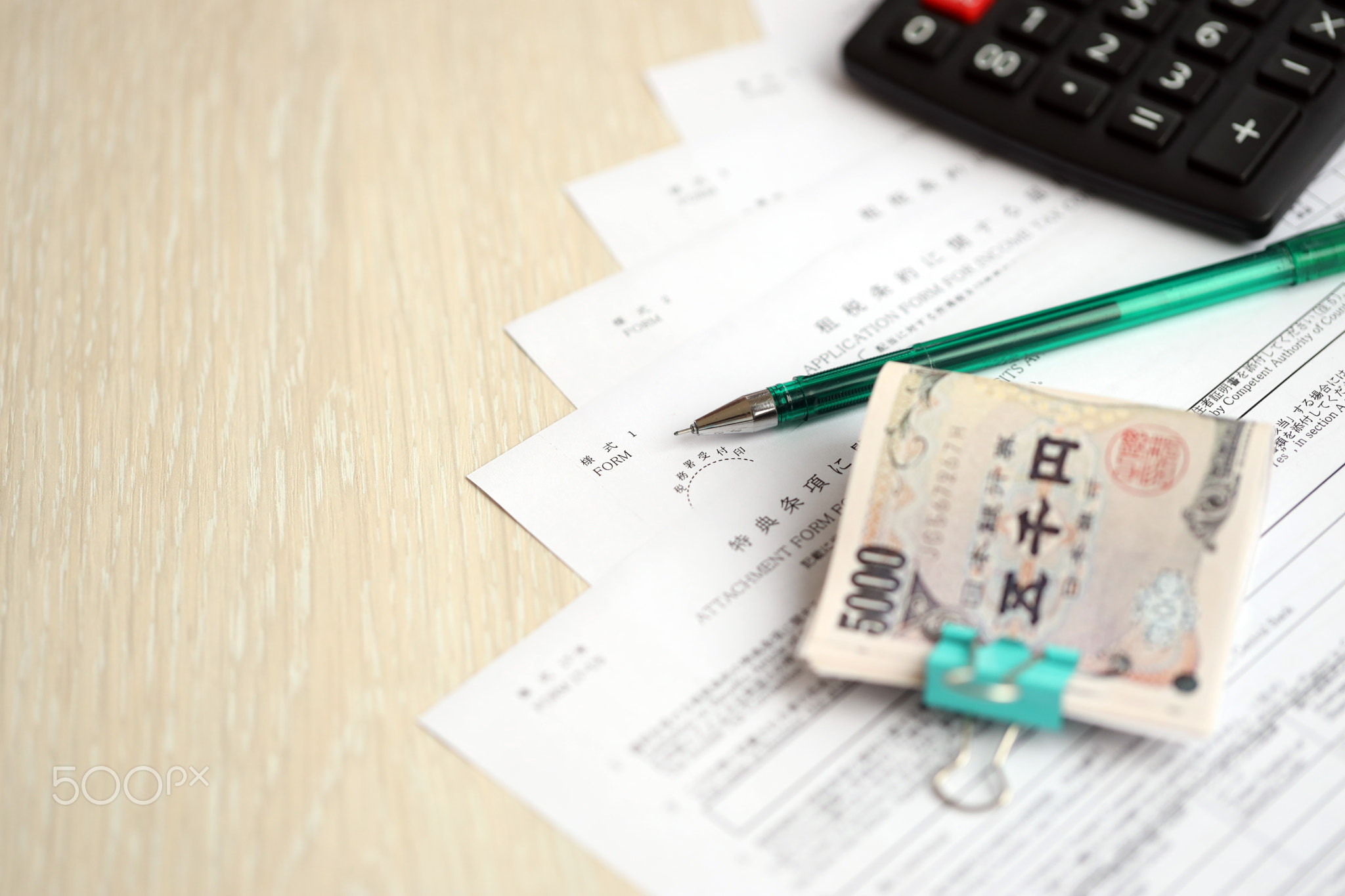 Japanese tax forms lies on table with calculator, pen and japanese yen money bills roll