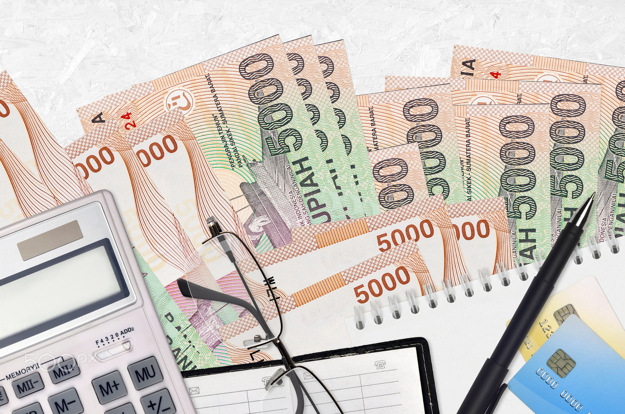 5000 Indonesian rupiah bills and calculator with glasses and pen. Tax payment concept or investment