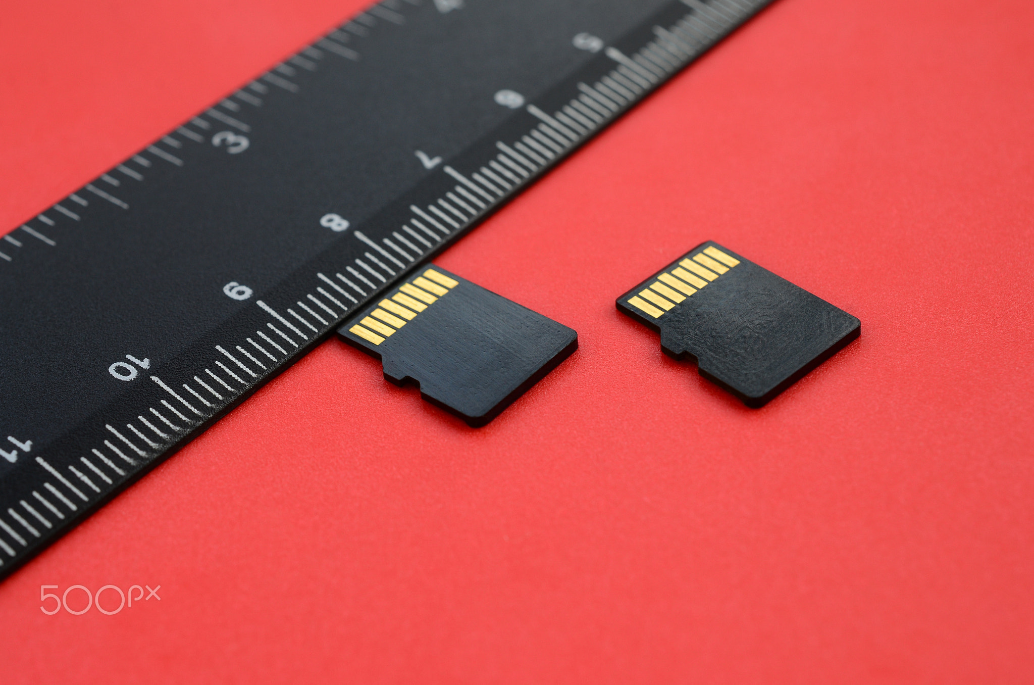 Two small micro SD memory cards lie on a red background next to a black ruler. A small and compact