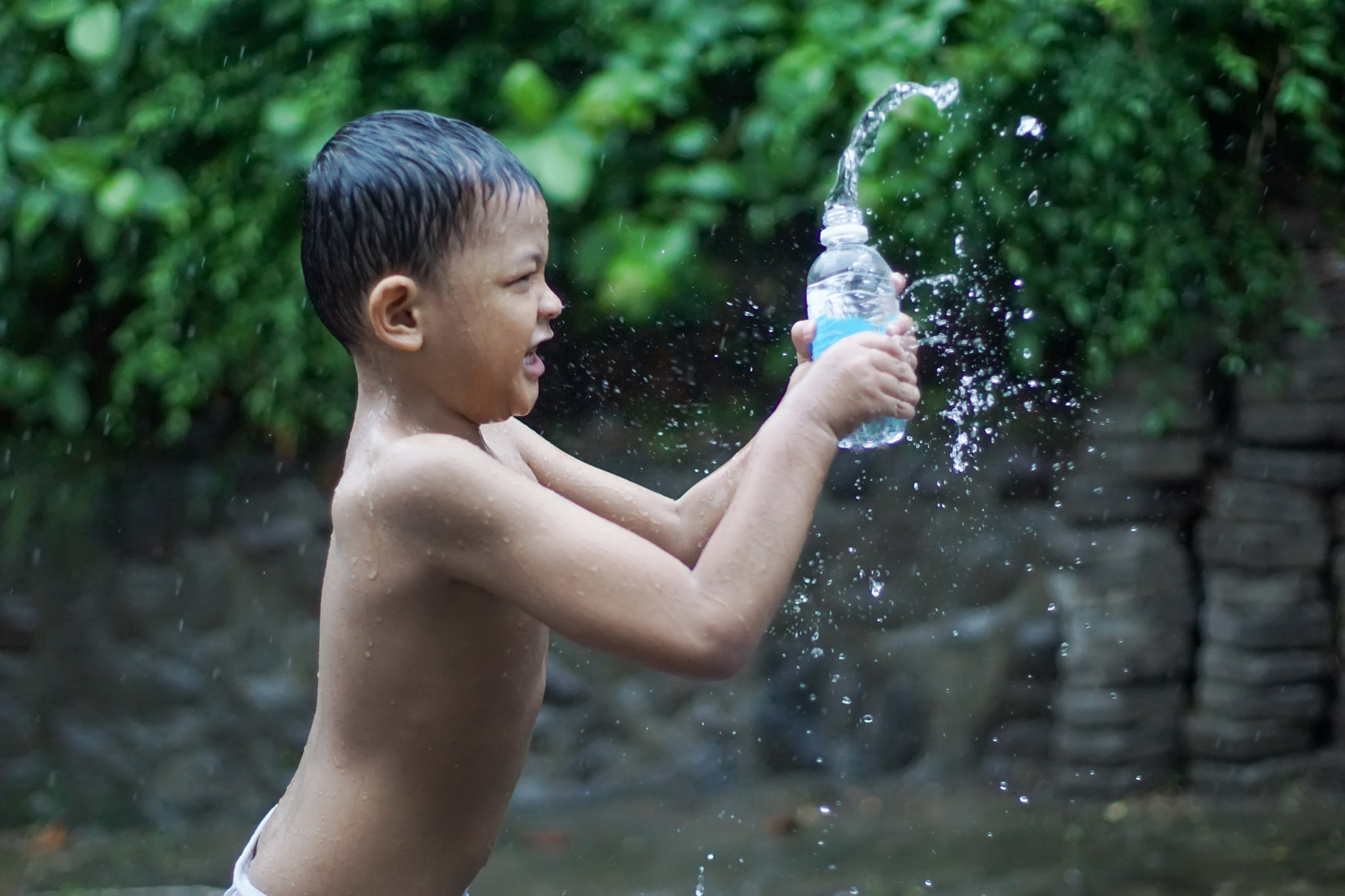 Side View of Shirtless Boy Playing Water on Back Yard