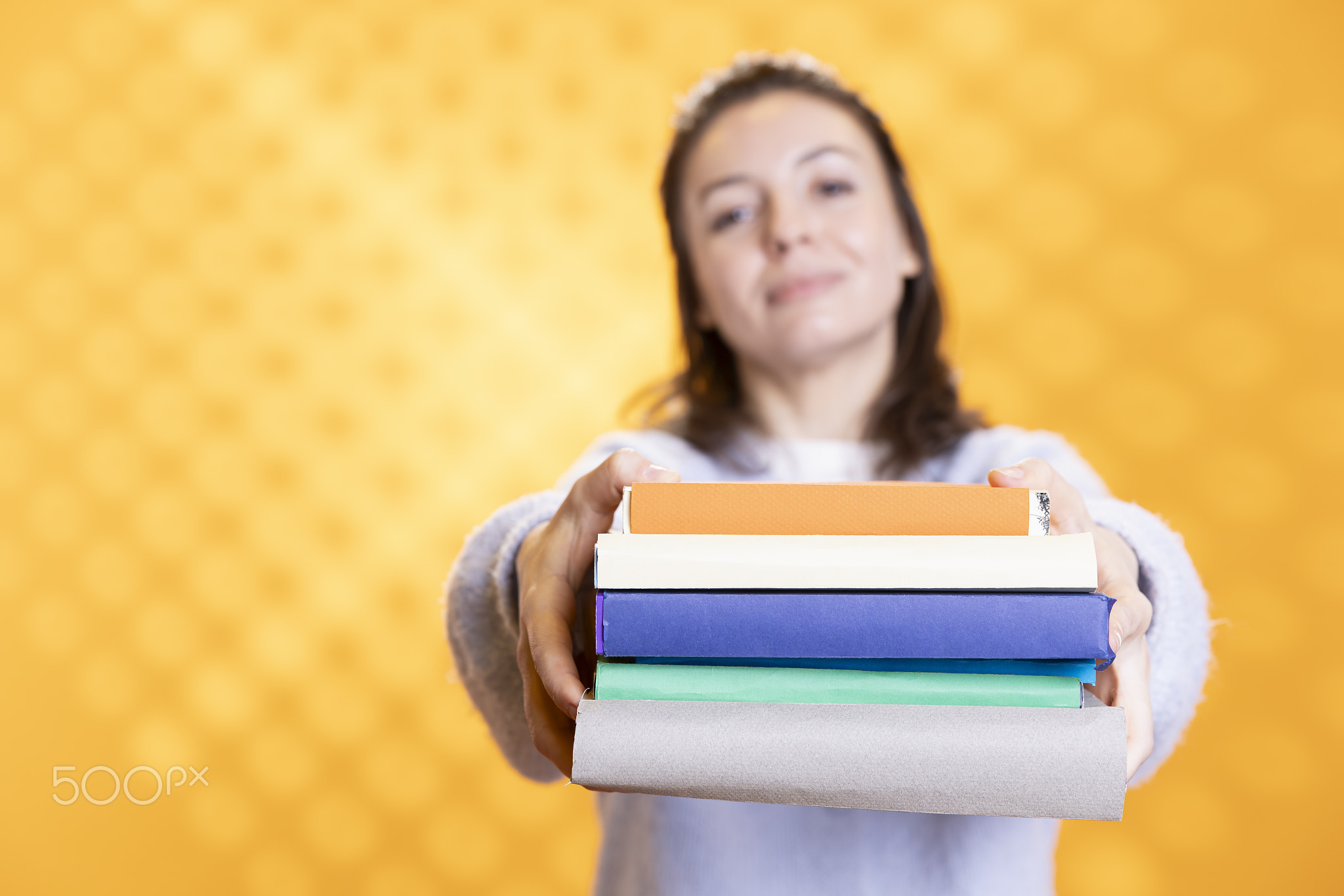 Portrait of smiling woman offering pile of books, recommending reading