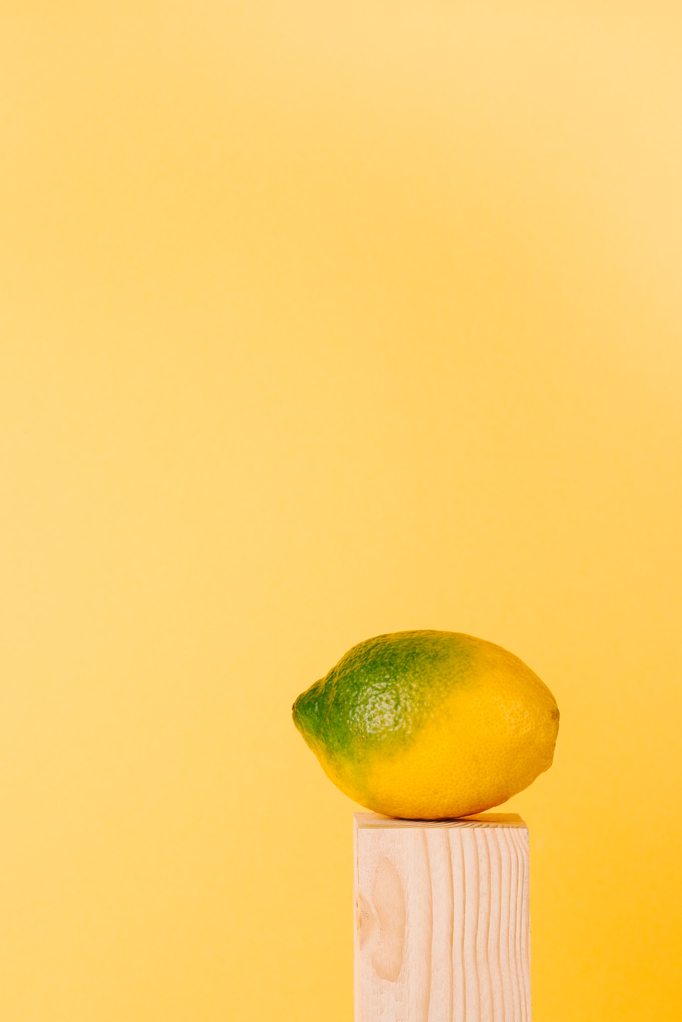 yellow and green lemon on wood pedestal on yellow background