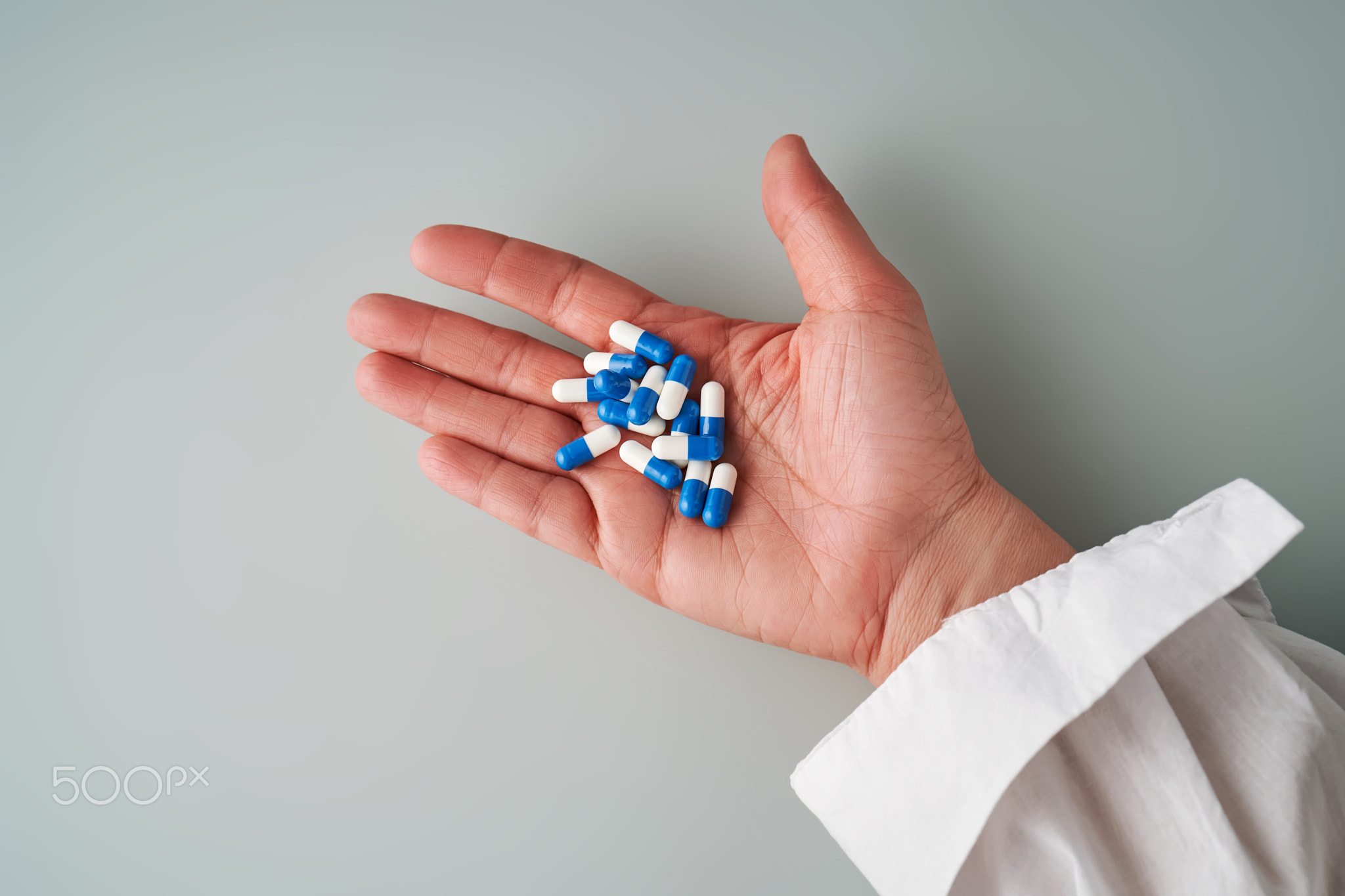 A hand holds a handful of white and blue pills on a blue background.