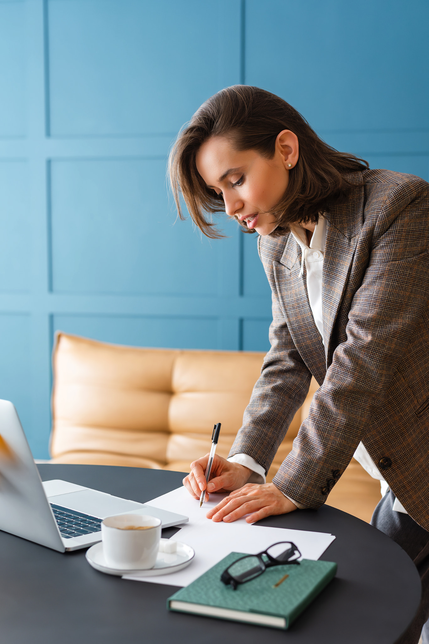 Beautiful brunette woman standing at desk, holding pen and working with documents.