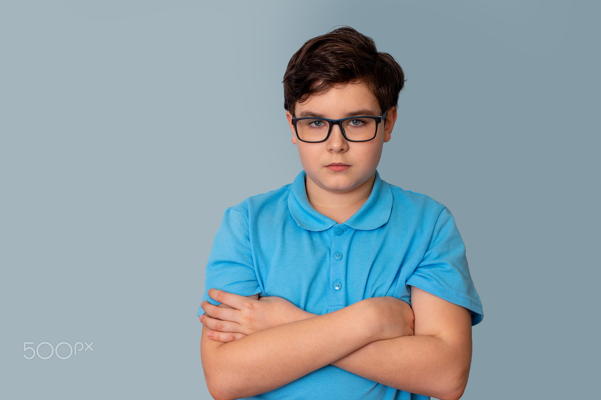 A sad dark-haired boy with glasses,arms crossed on his chest