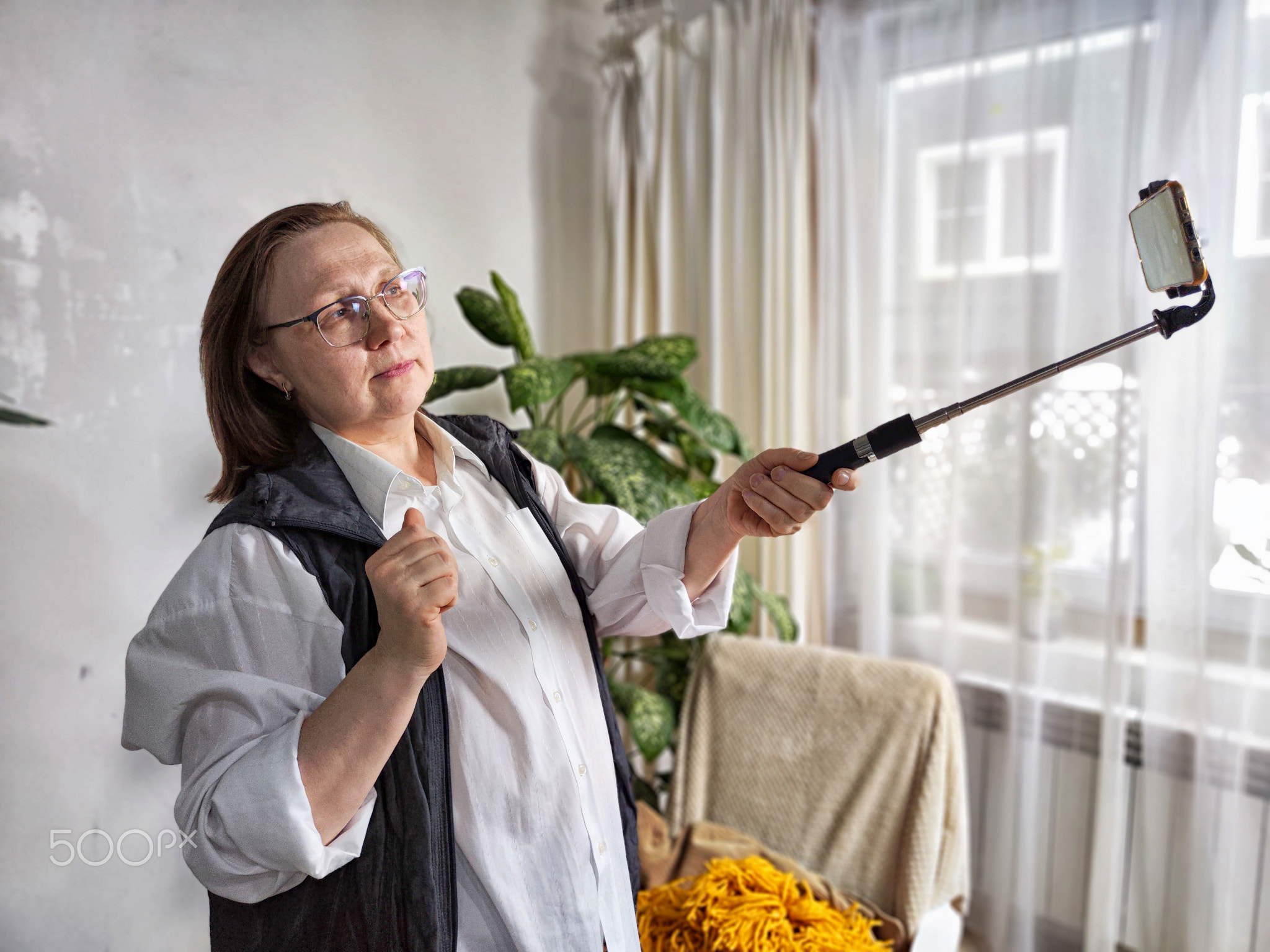 Middle aged woman takes a selfie with a selfie stick in her home