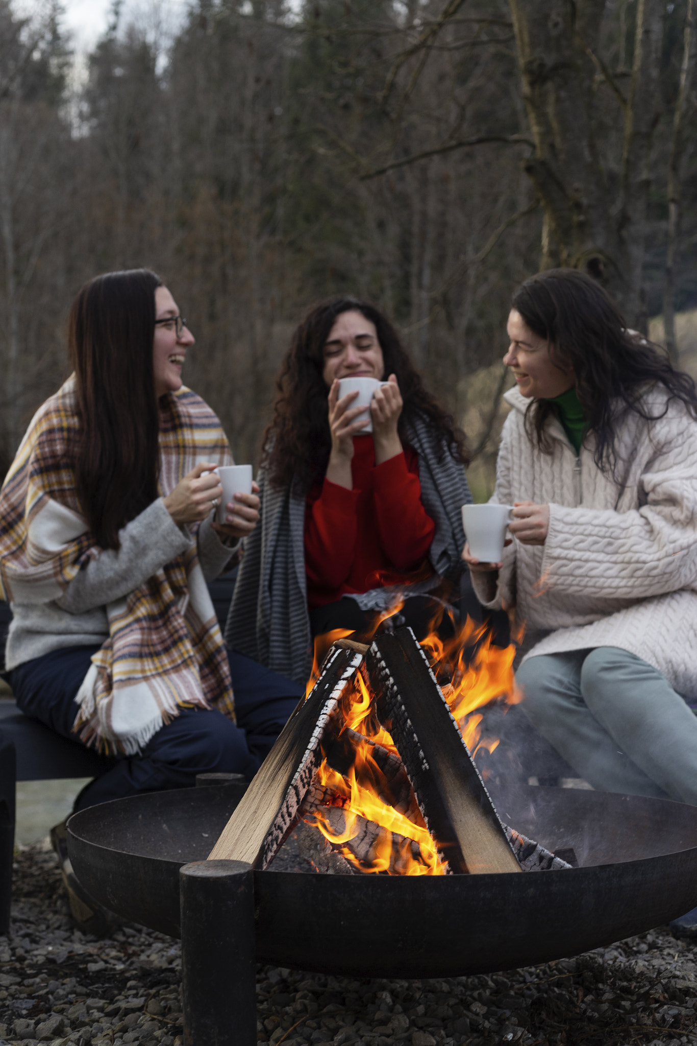 Three Women Enjoying a Bonfire in a Forest Setting