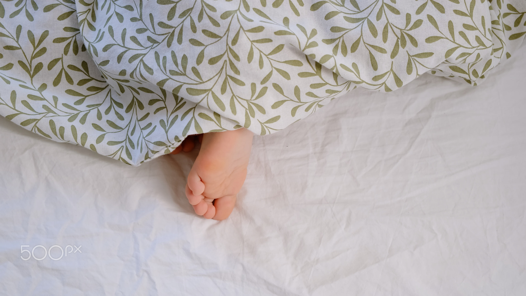 The child's bare foot sticking out from under the blanket. The kid