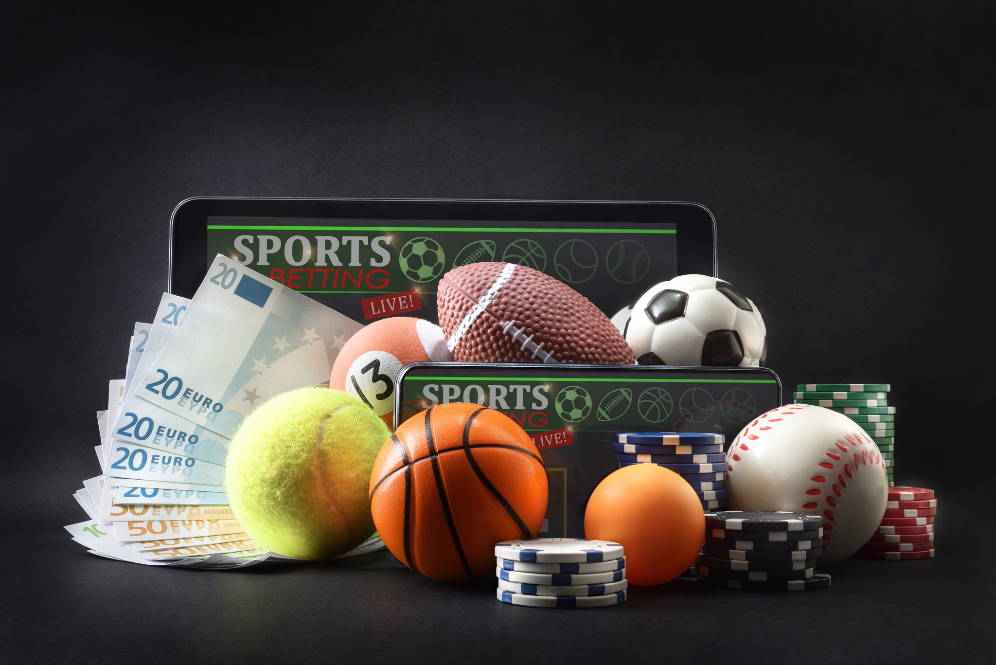 Concept of physical and online sports betting with balls representing various sports on a dark isola