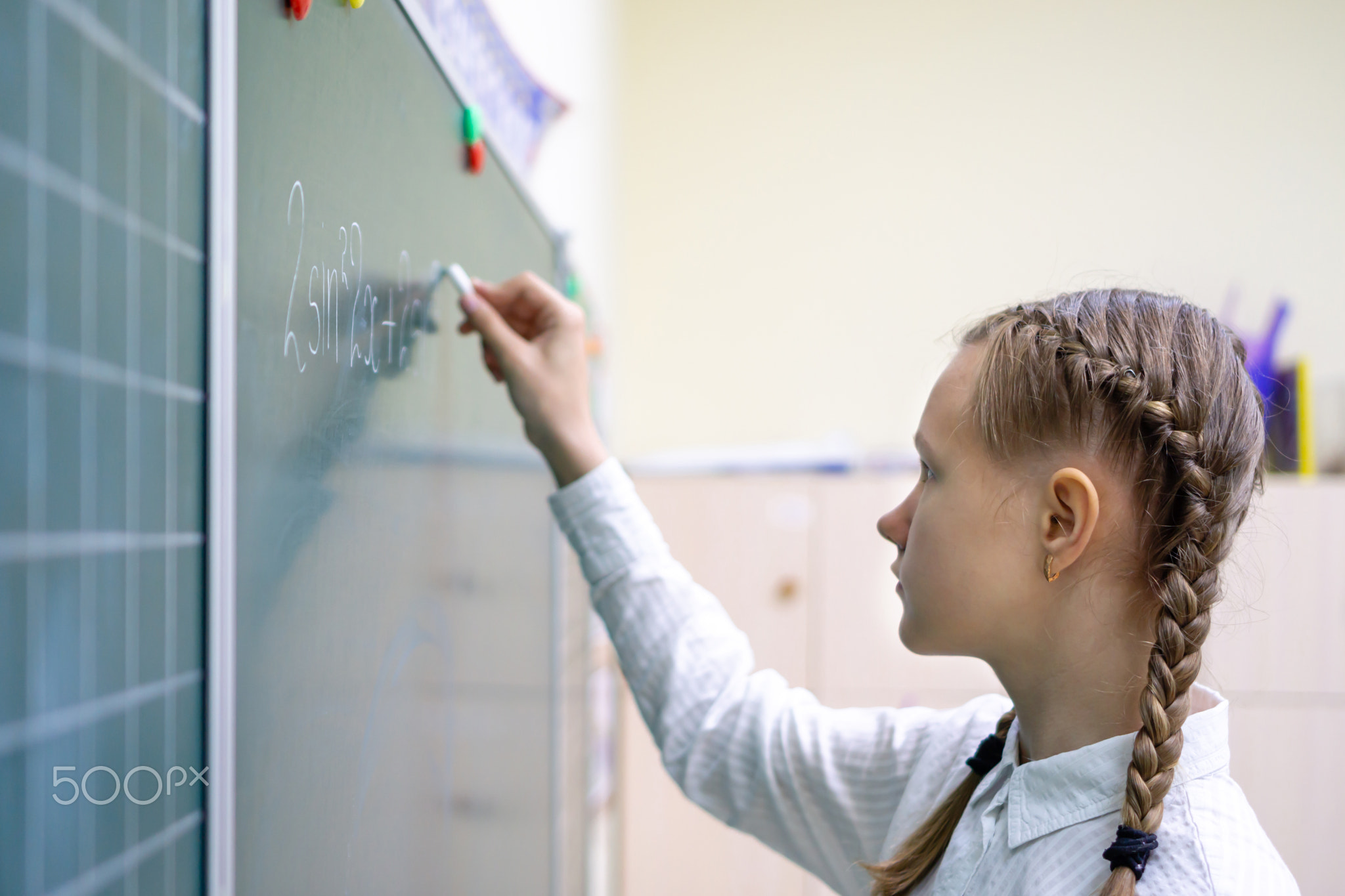 Portrait of a Caucasian schoolgirl writing with chalk on a blackboard. A thoughtful child on the