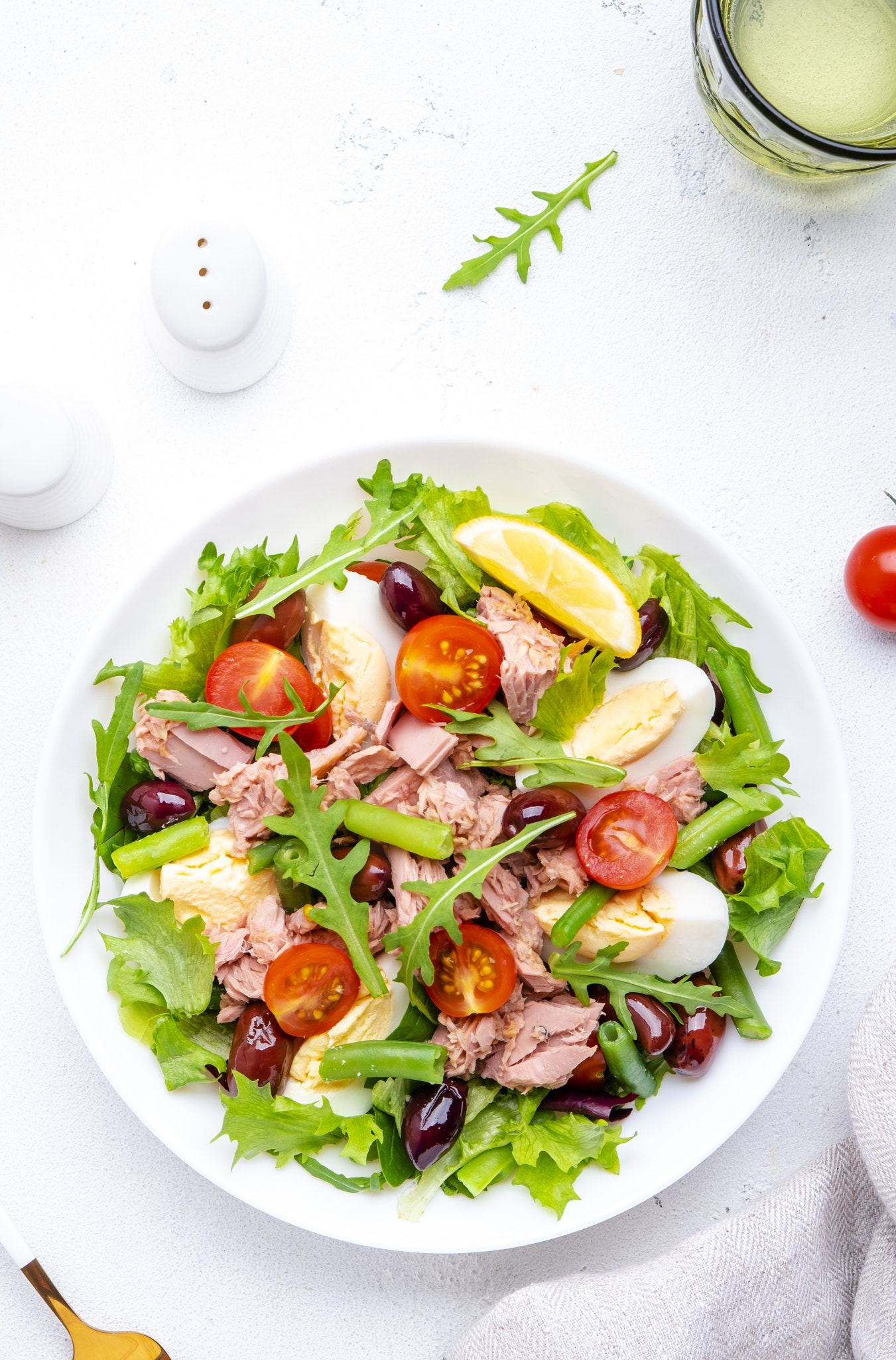 Tasty salad with tuna, tomatoes, eggs, beans, lettuce and olives with mustard dressing on white back