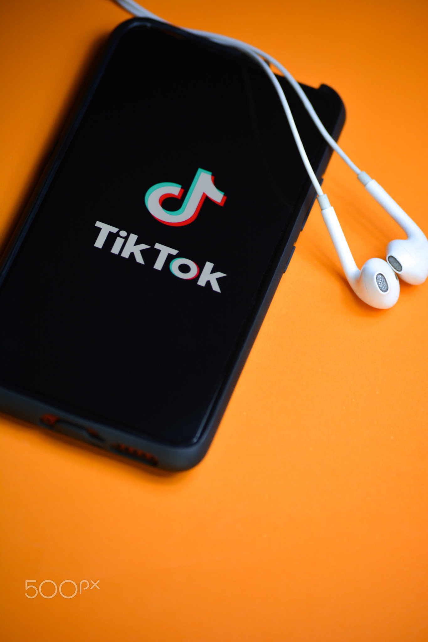 Tik Tok application icon on mobile phone screen with earphones.