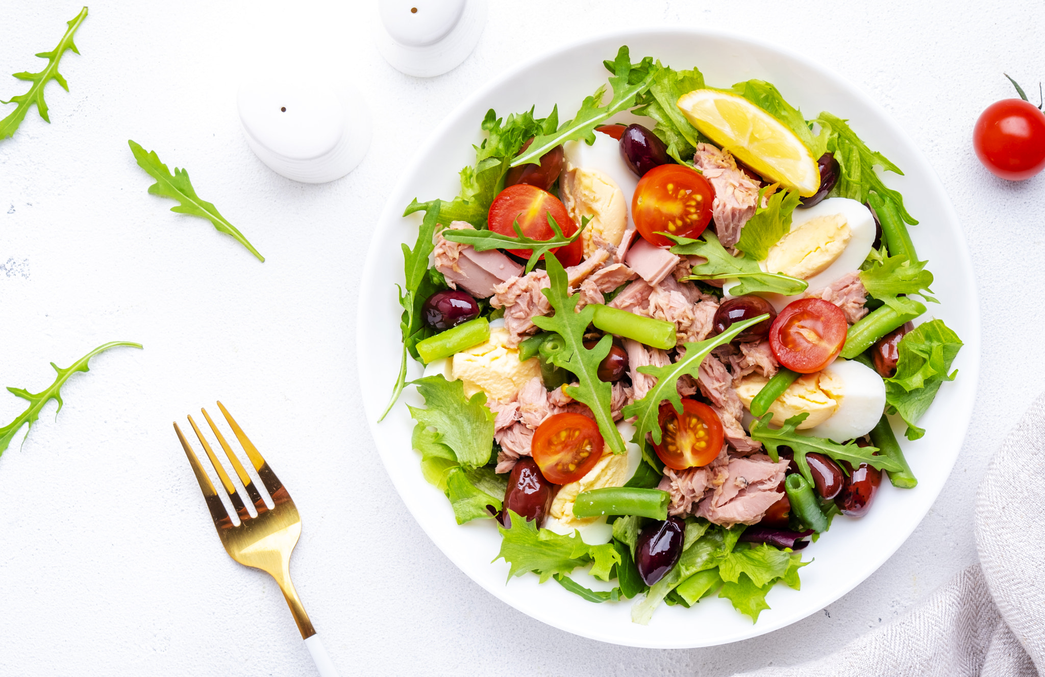 Tasty salad with tuna, tomatoes, eggs, beans, lettuce and olives on white background, top view