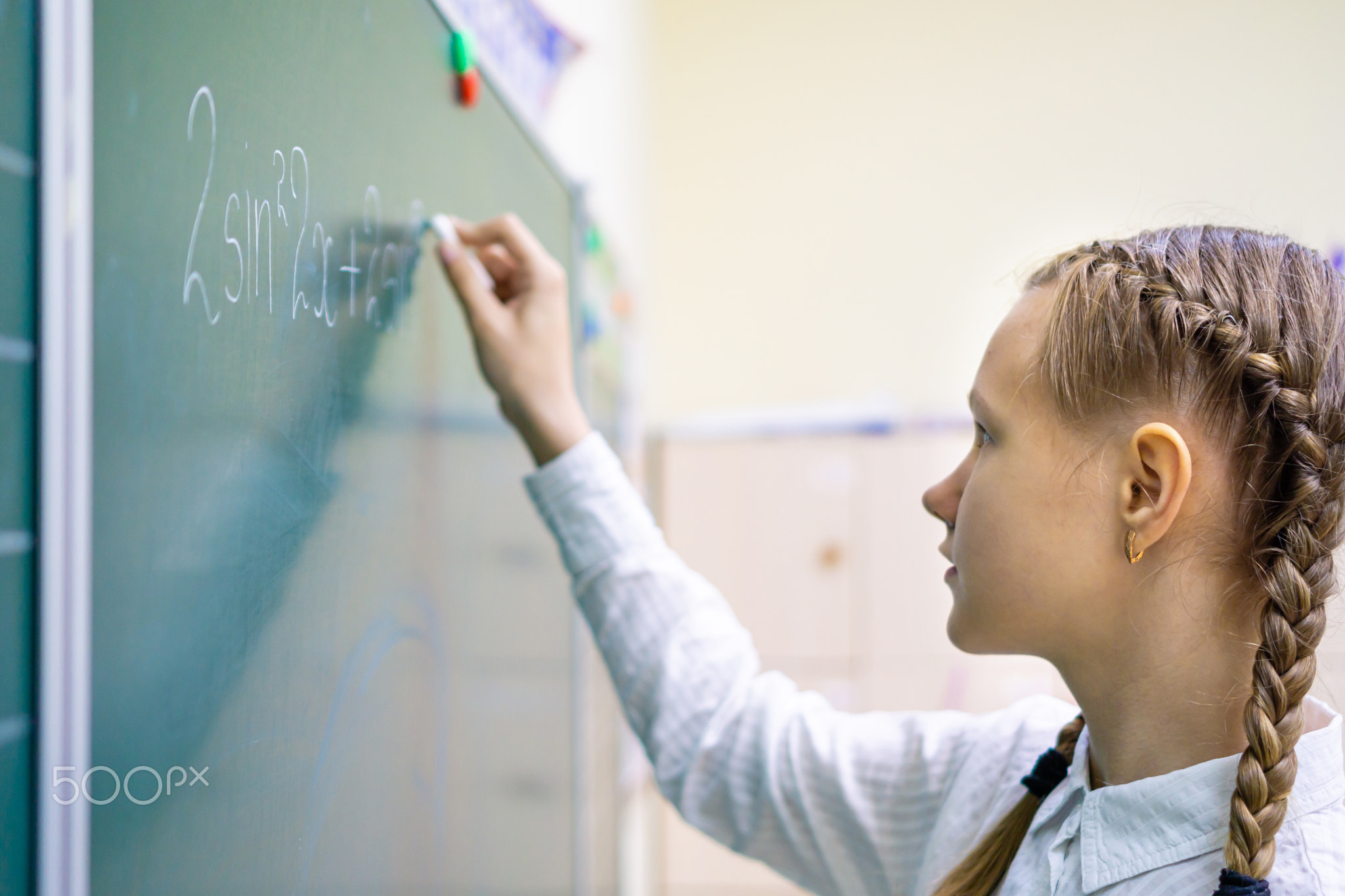 A young student standing at the blackboard and solving mathematical equations and problems during