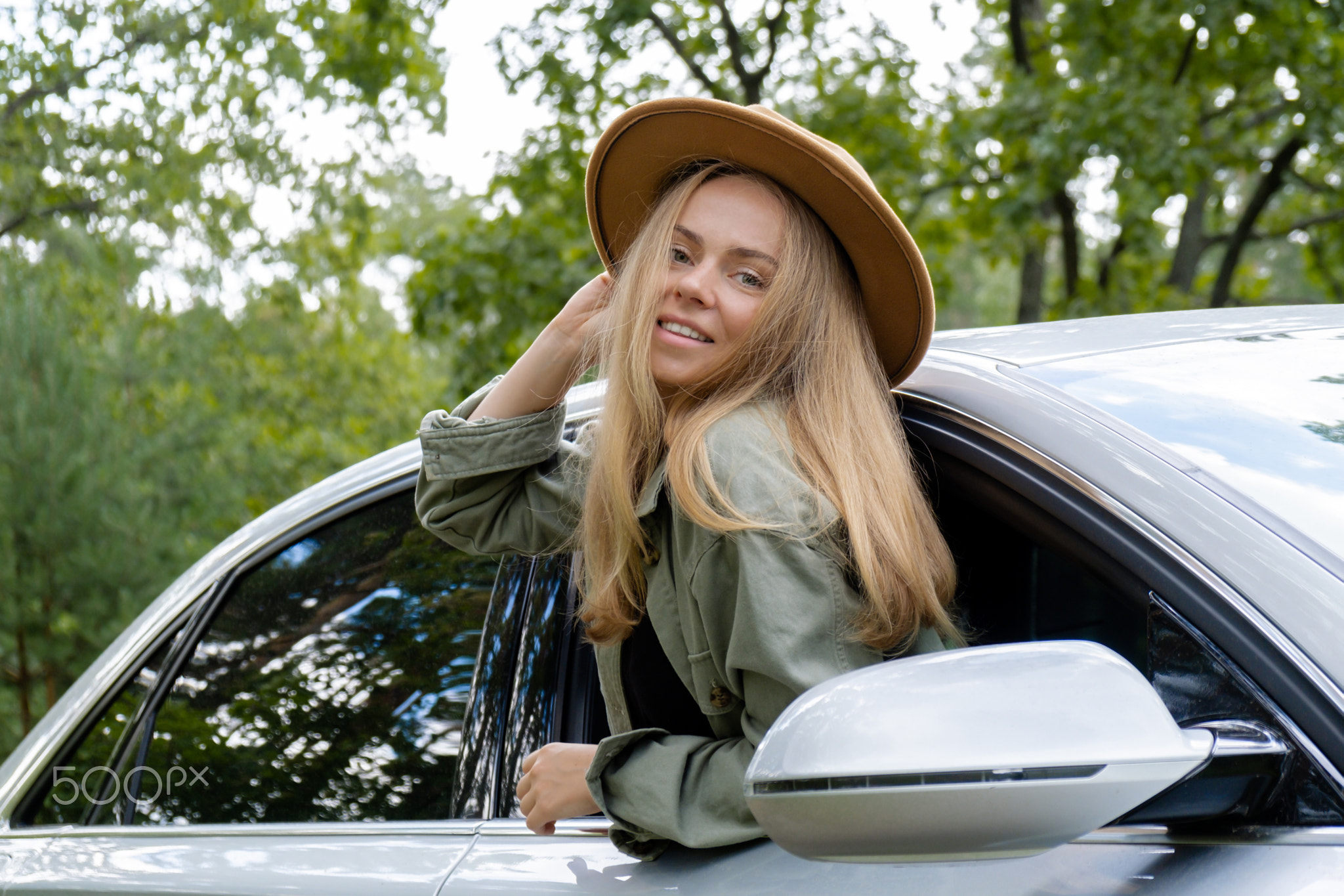 Smiling young woman in hat looking from car window. Local solo travel