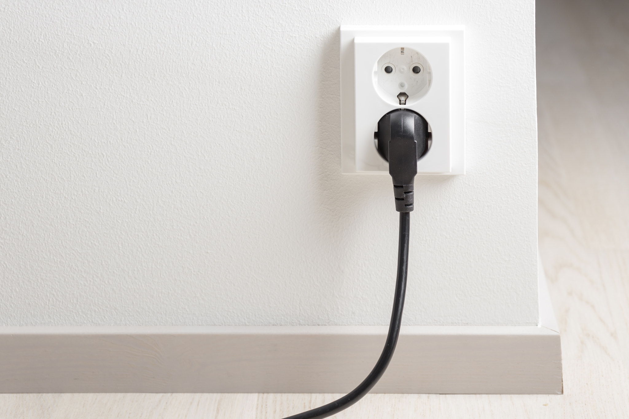 A close-up of a double electrical outlet mounted on a white wall, with a power cord plugged into one