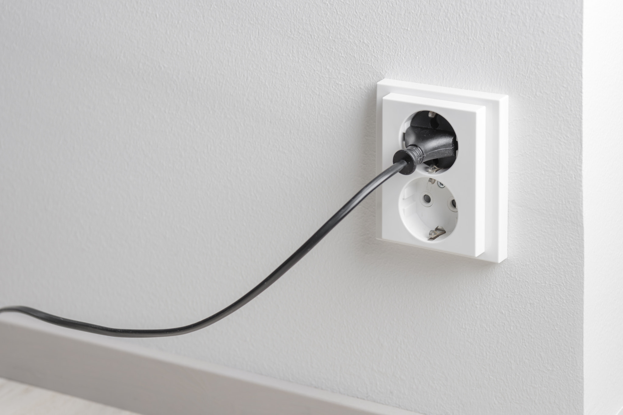 A close-up of a double electrical outlet mounted on a white wall, with a power cord plugged into one