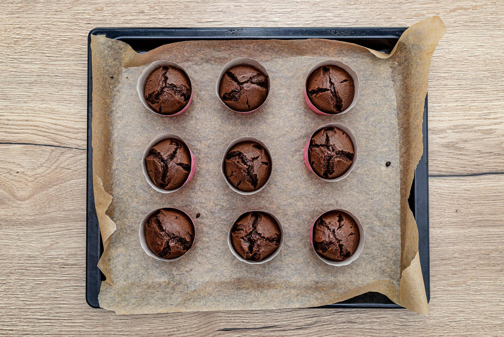 Brown chocolate muffins wrapped in white paper baked in the oven, lying on baking paper, top view.