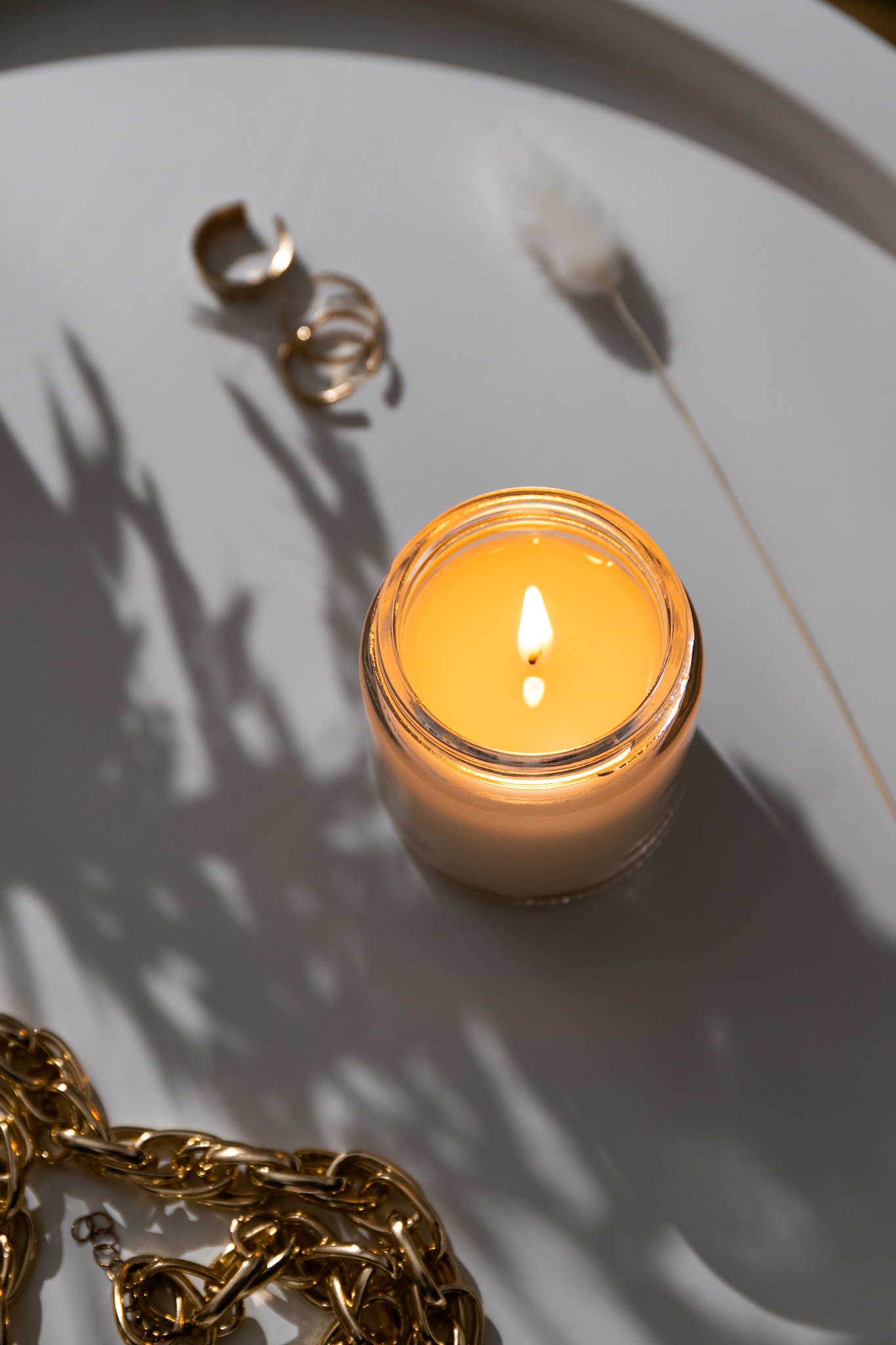 White burning candle on coffee table with gold jewelry accessories, home decorations