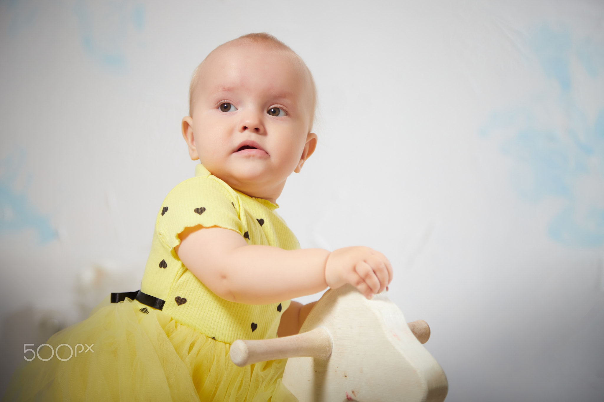 Baby dressed in yellow tulle skirt plays on a white rocking horse