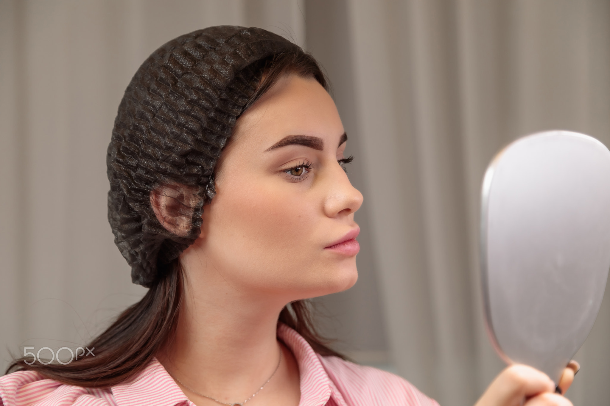 Beautician looking at mirror checking eyebrows after treatment in beauty salon