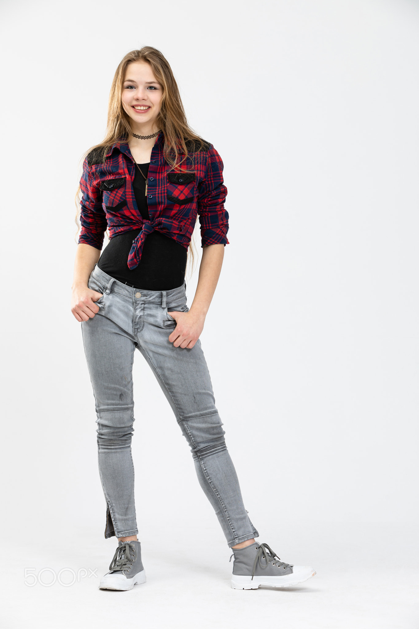 A confident girl stands with her hands tucked in the pockets of her pants.
