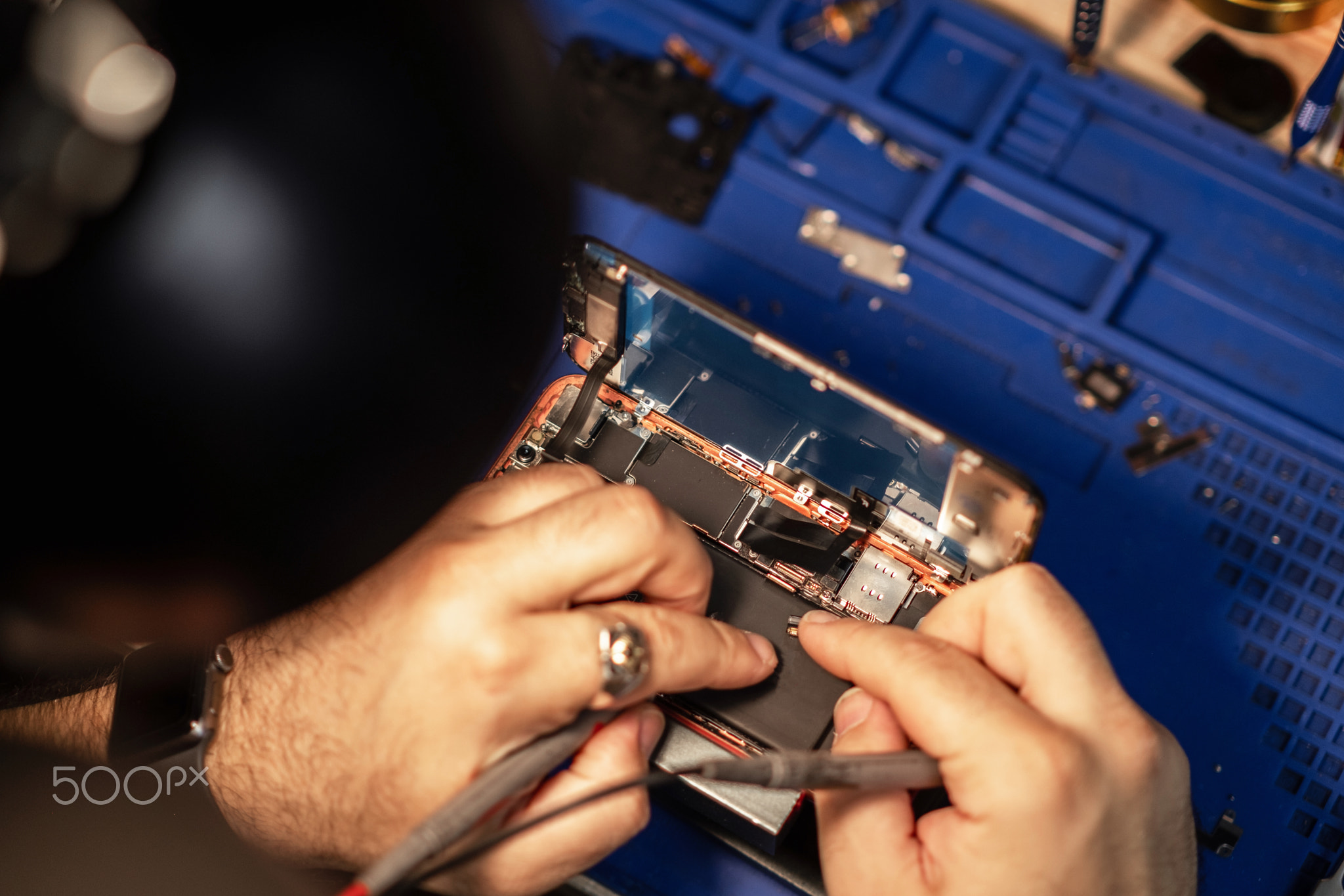 Technician performing smartphone battery repair in a workshop with tools and components while