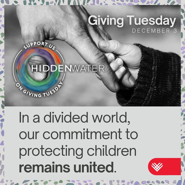 A black-and-white photo of two hands holding each other—a child’s hand being gently held by an adult’s hand. The text reads: “In a divided world, our commitment to protecting children remains united. Giving Tuesday, December 3.”