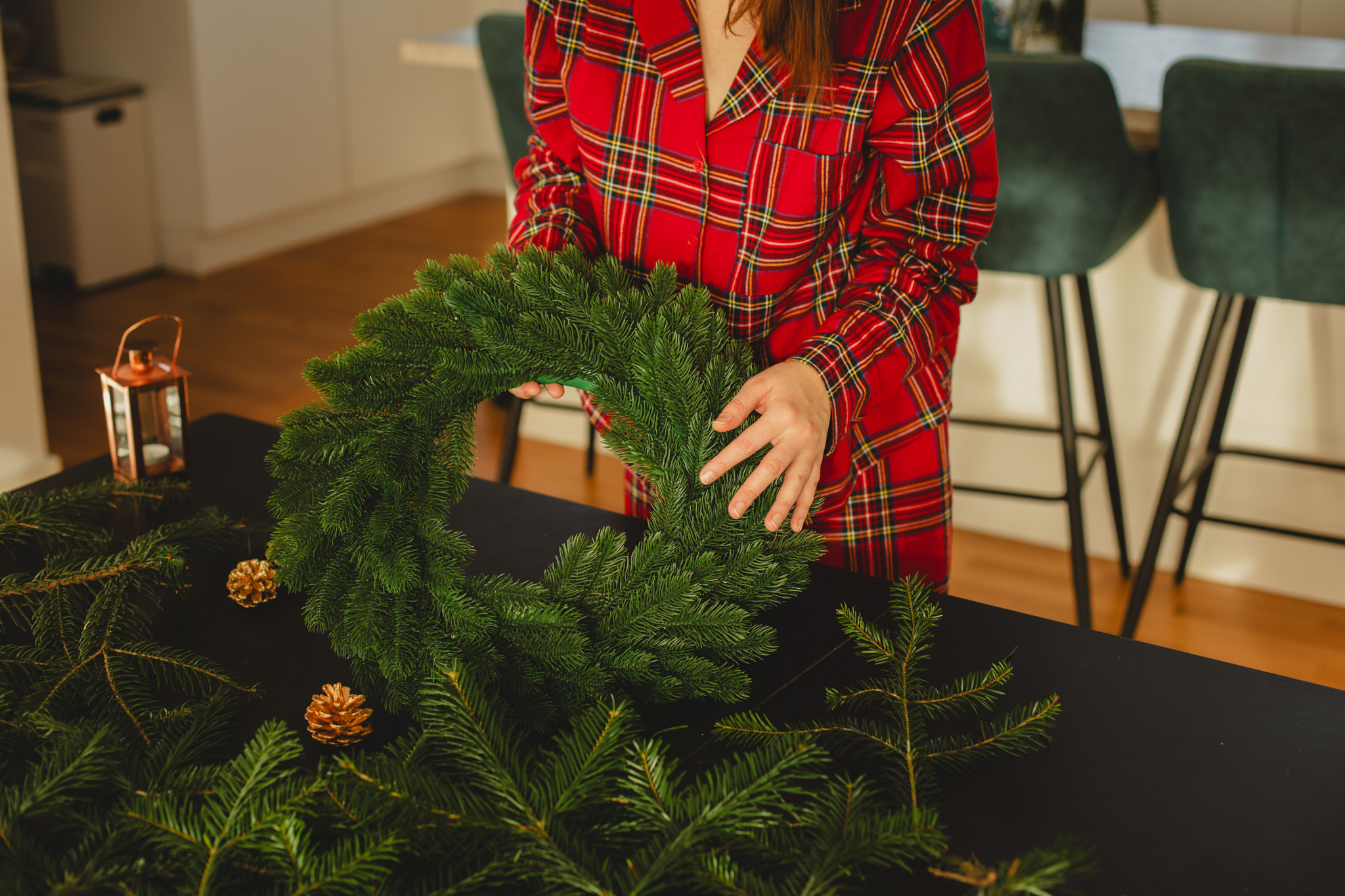 Holiday Preparations: Artistic Decoration of a Christmas Wreath by a Woman in a Warm Atmosphere