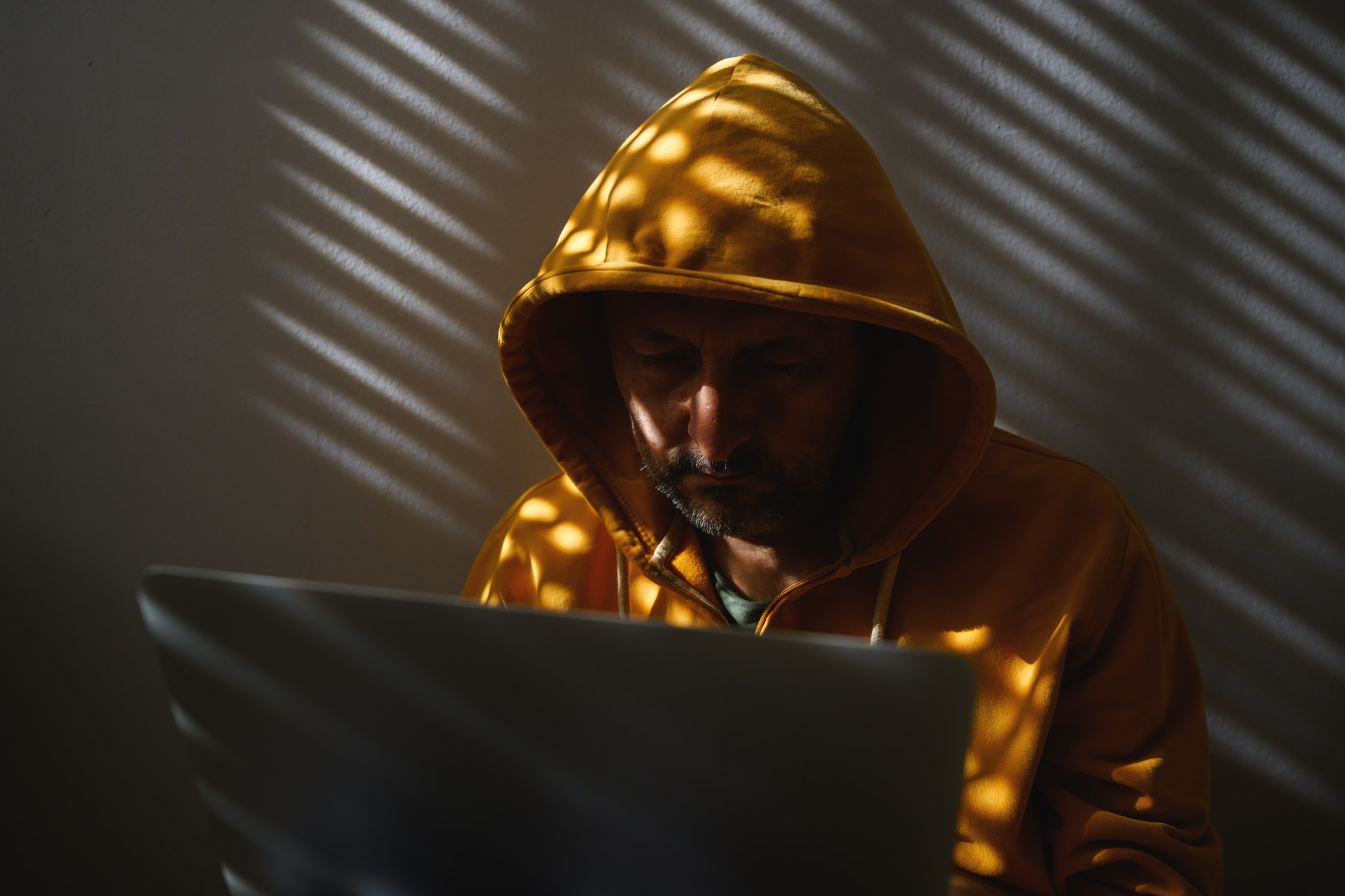 Computer hacker wearing yellow hoodie using laptop