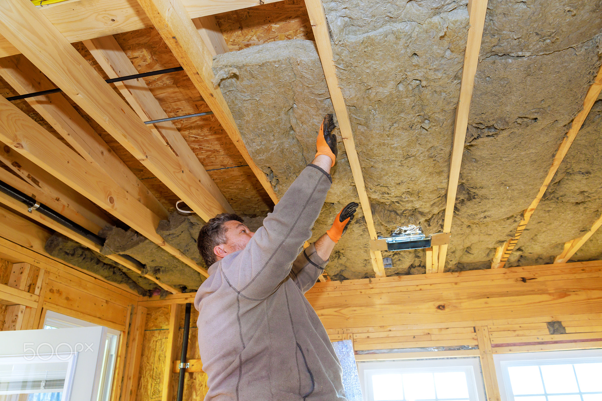 Worker installing insulation in wooden ceiling during home renovation
