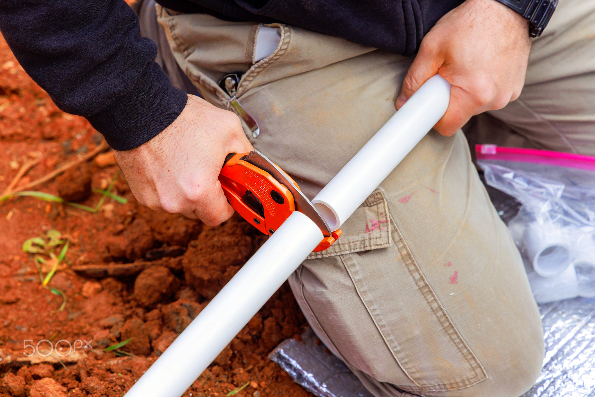 Construction worker cuts PVC pipe to size for plumbing installation in