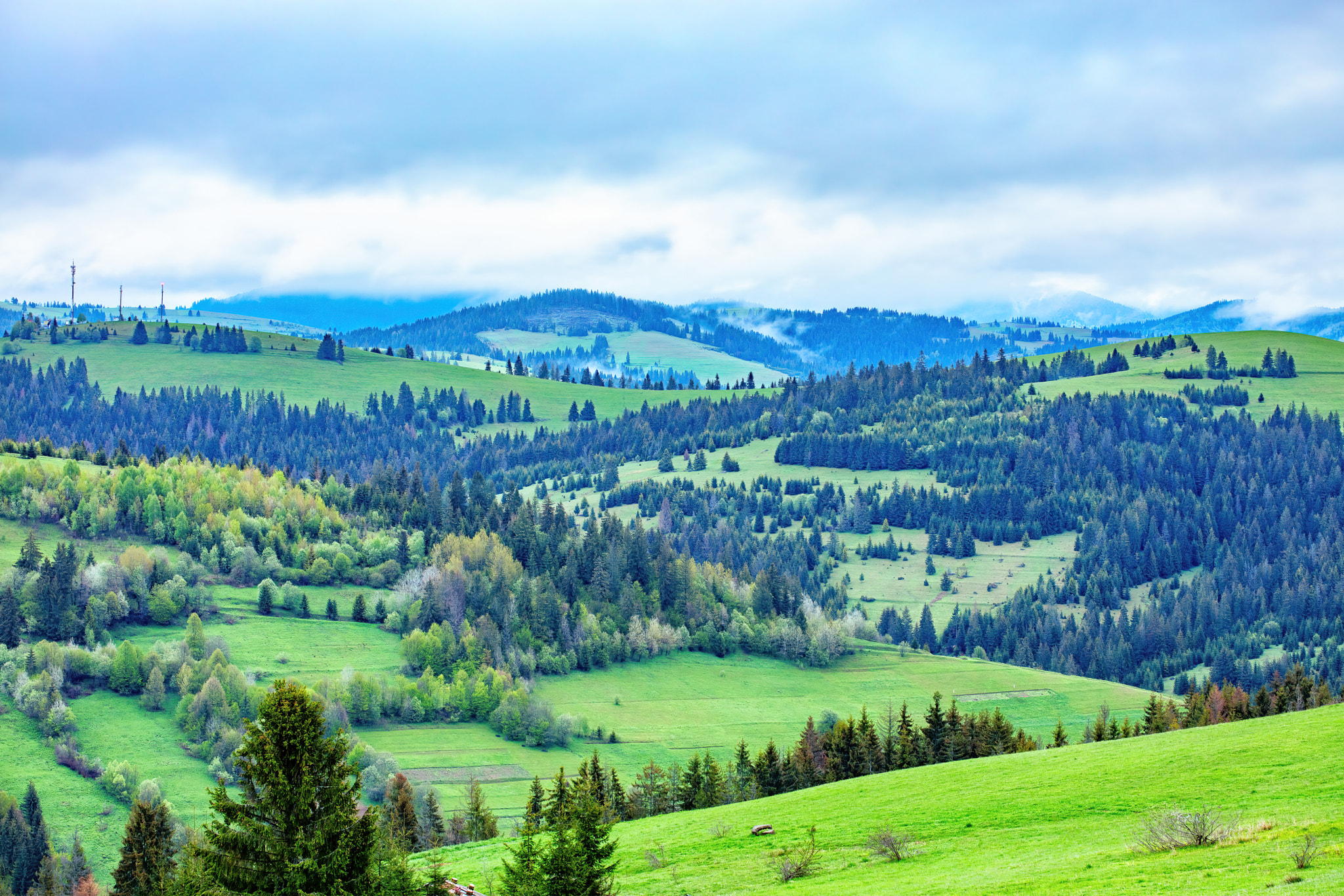 Lush green hills embrace the tranquil sky in a serene landscape of rolling mountains