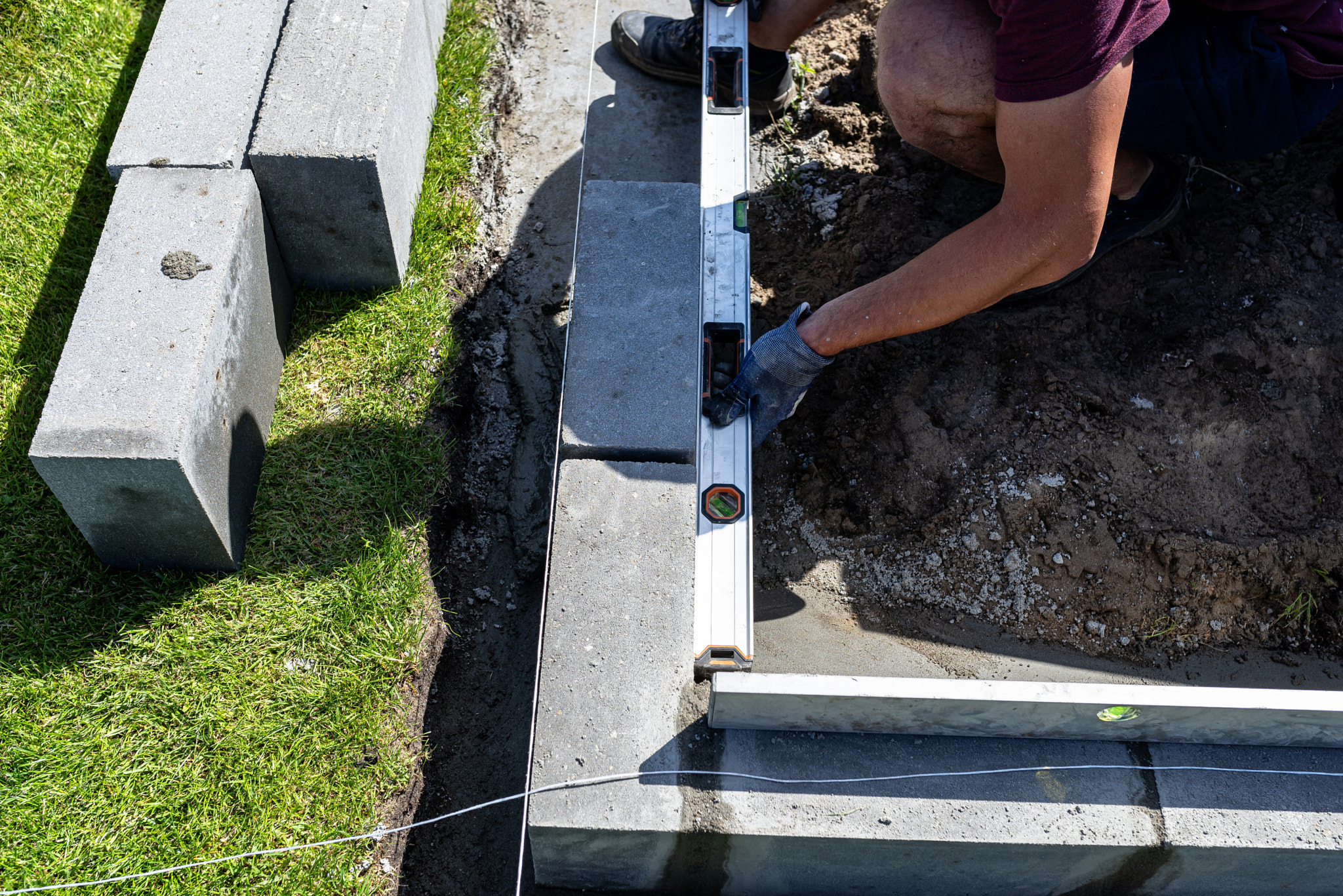 A man lays concrete blocks on a poured foundation, gluing them with mortar.