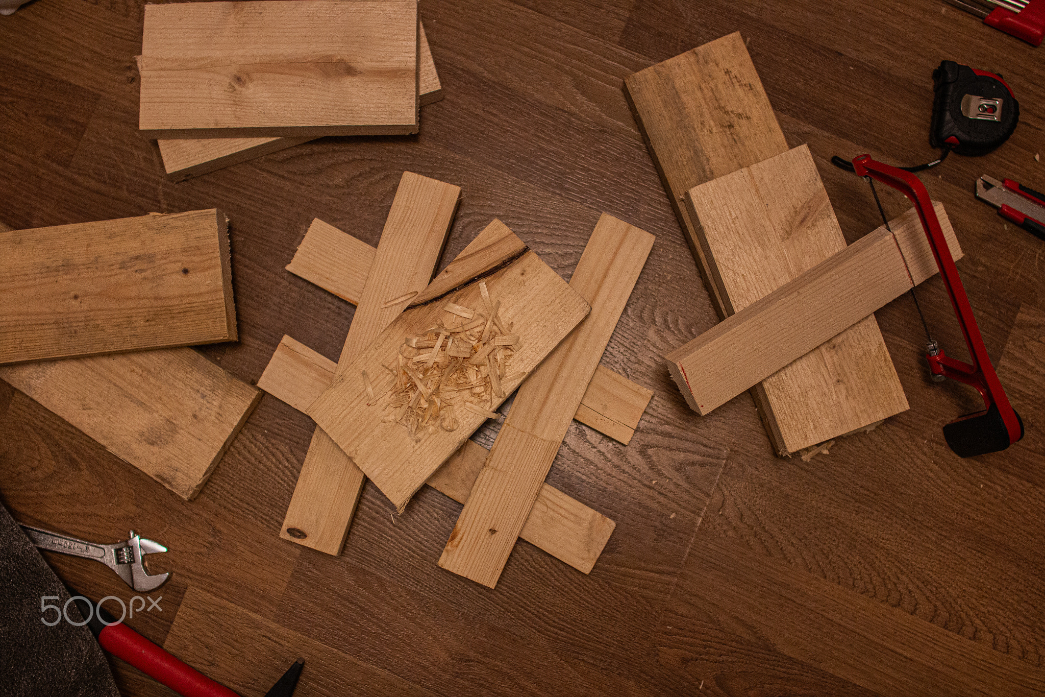 Wooden planks, shavings, a red-handled saw, a wrench, and a tape measure