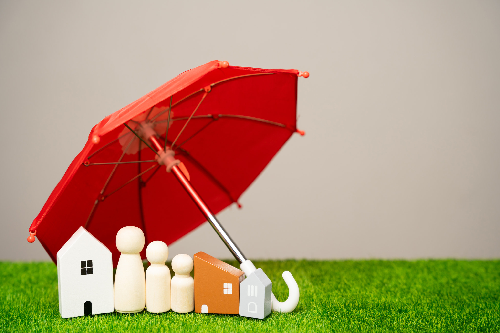 Property and family insurance concept. Miniature figures of a family stand near a houses and red umb