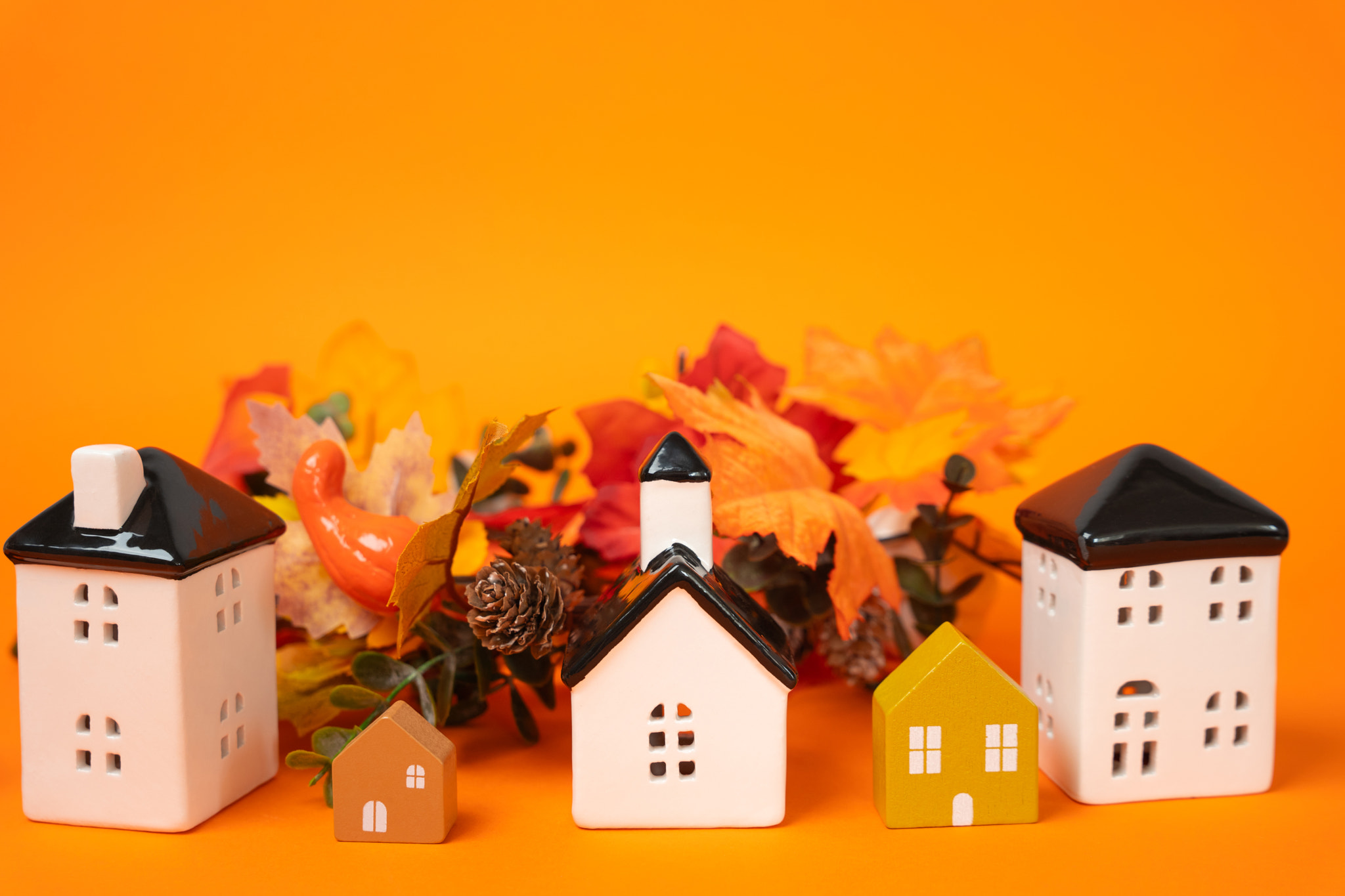 Miniature houses and autumn leaves on orange background. Autumn and real estate concept. Decor and d