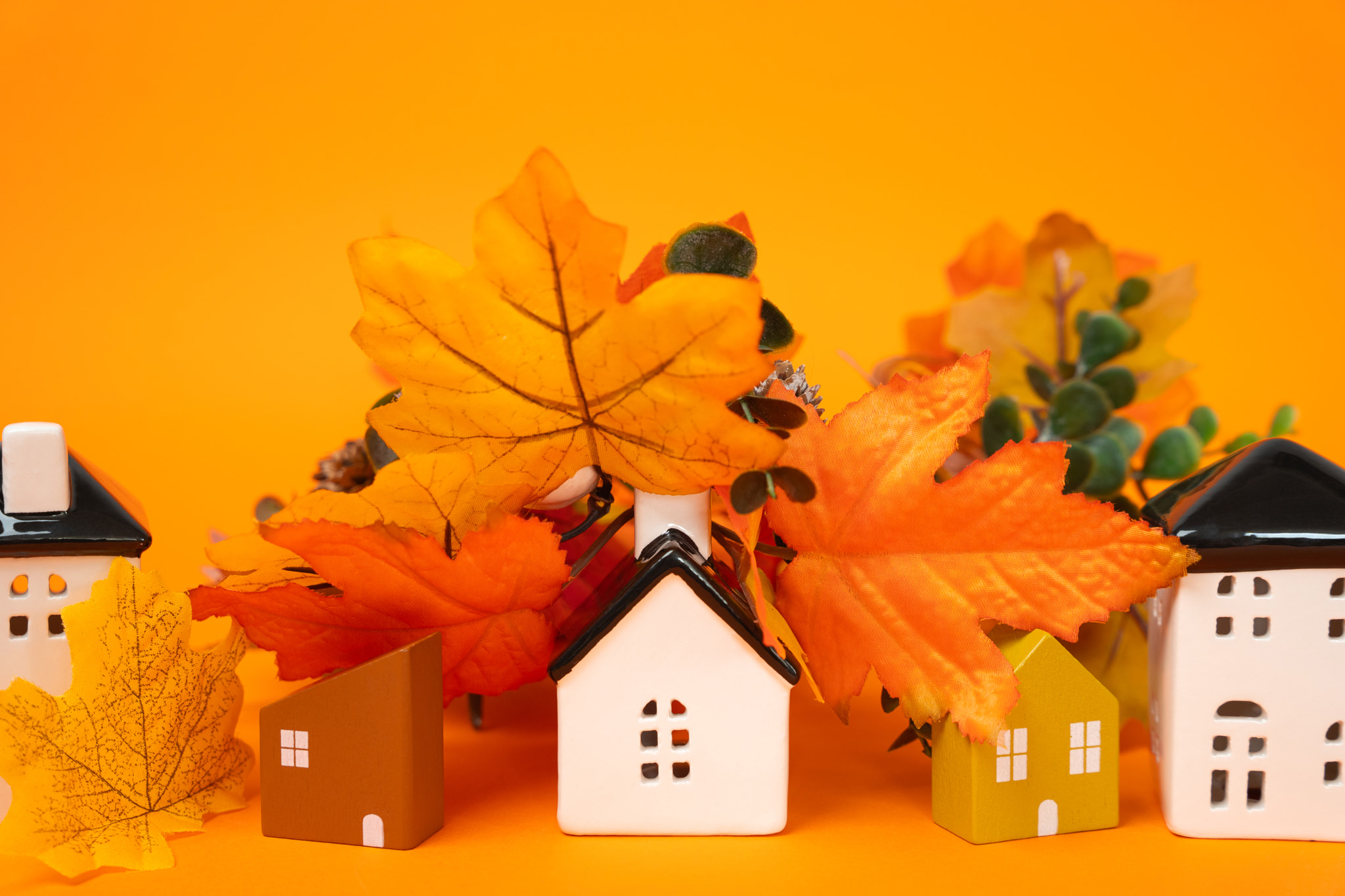 Miniature houses and autumn leaves on orange background. Autumn and real estate concept. Decor and d