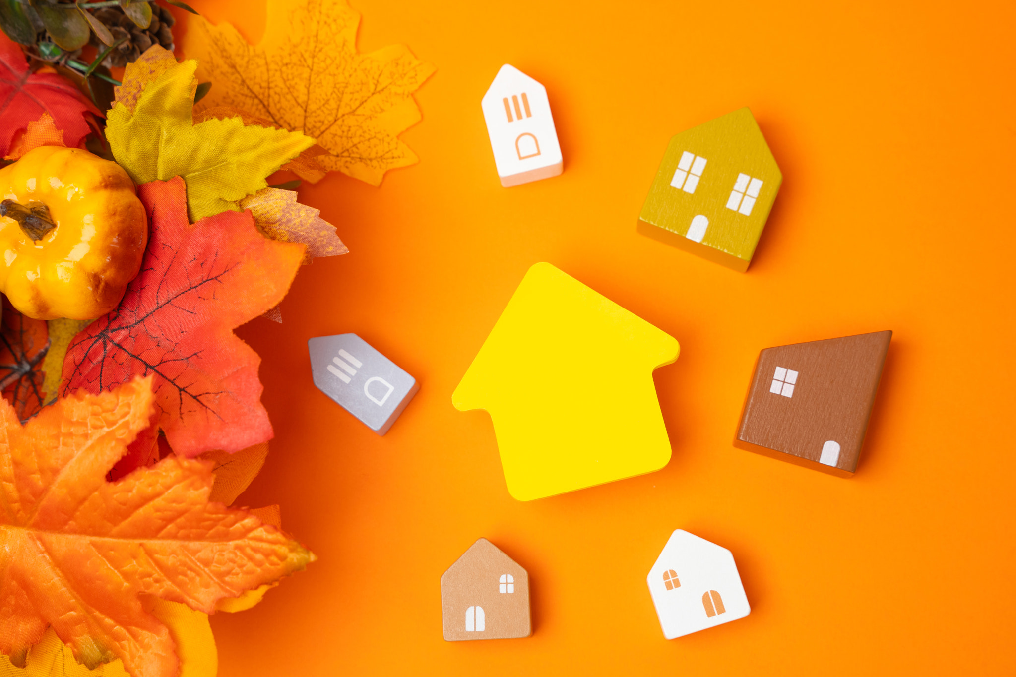 Miniature houses and autumn leaves on orange background. Autumn and real estate concept. Decor and d