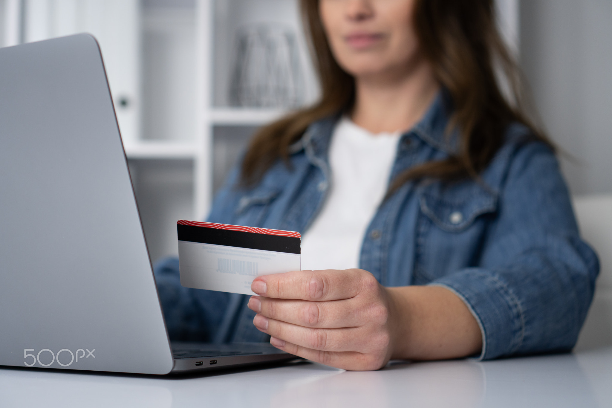 A woman is actively engaged in online shopping, utilizing her credit card and laptop to make