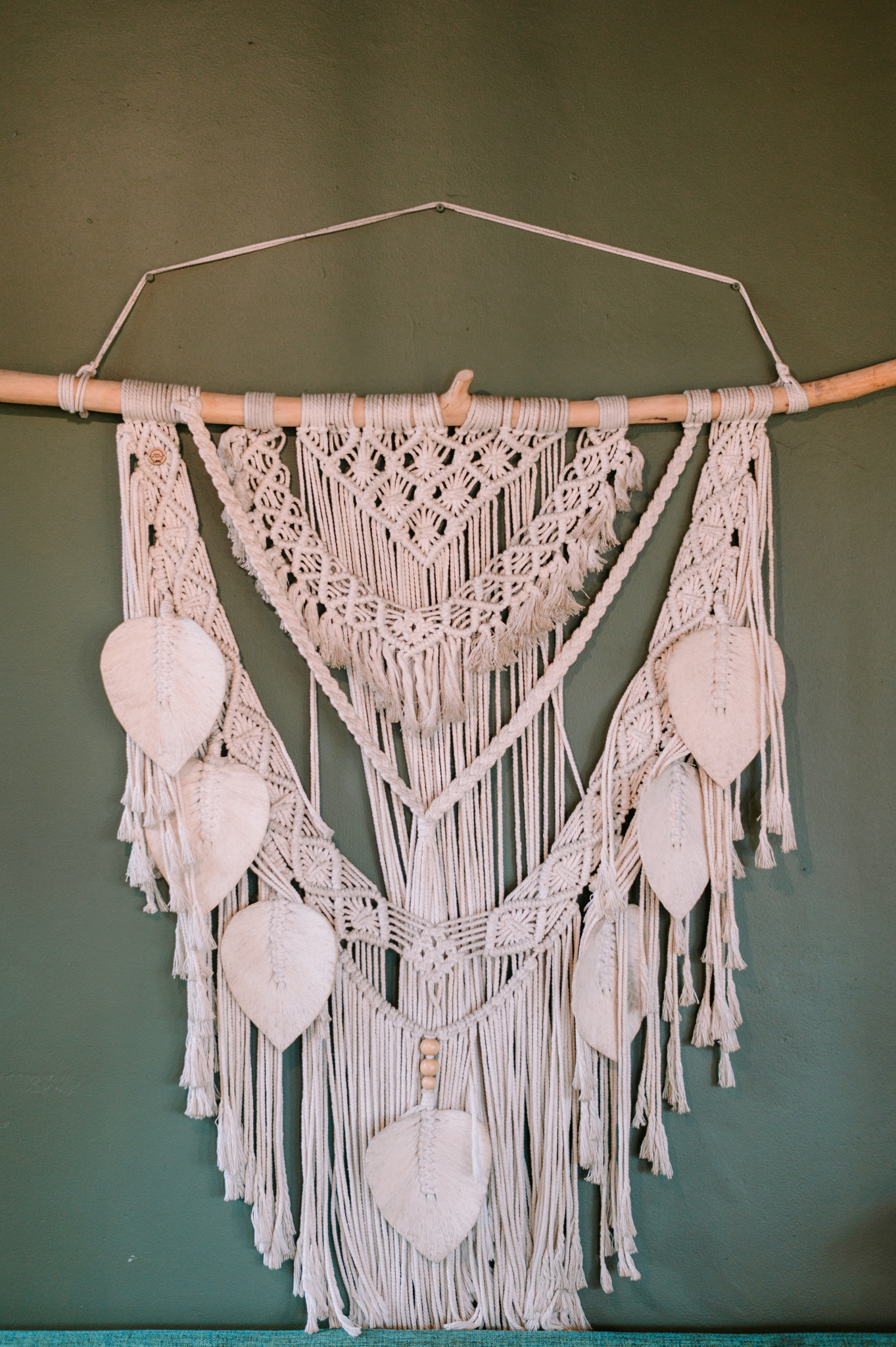 Handcrafted macrame wall hanging with delicate leaf embellishments on green wall