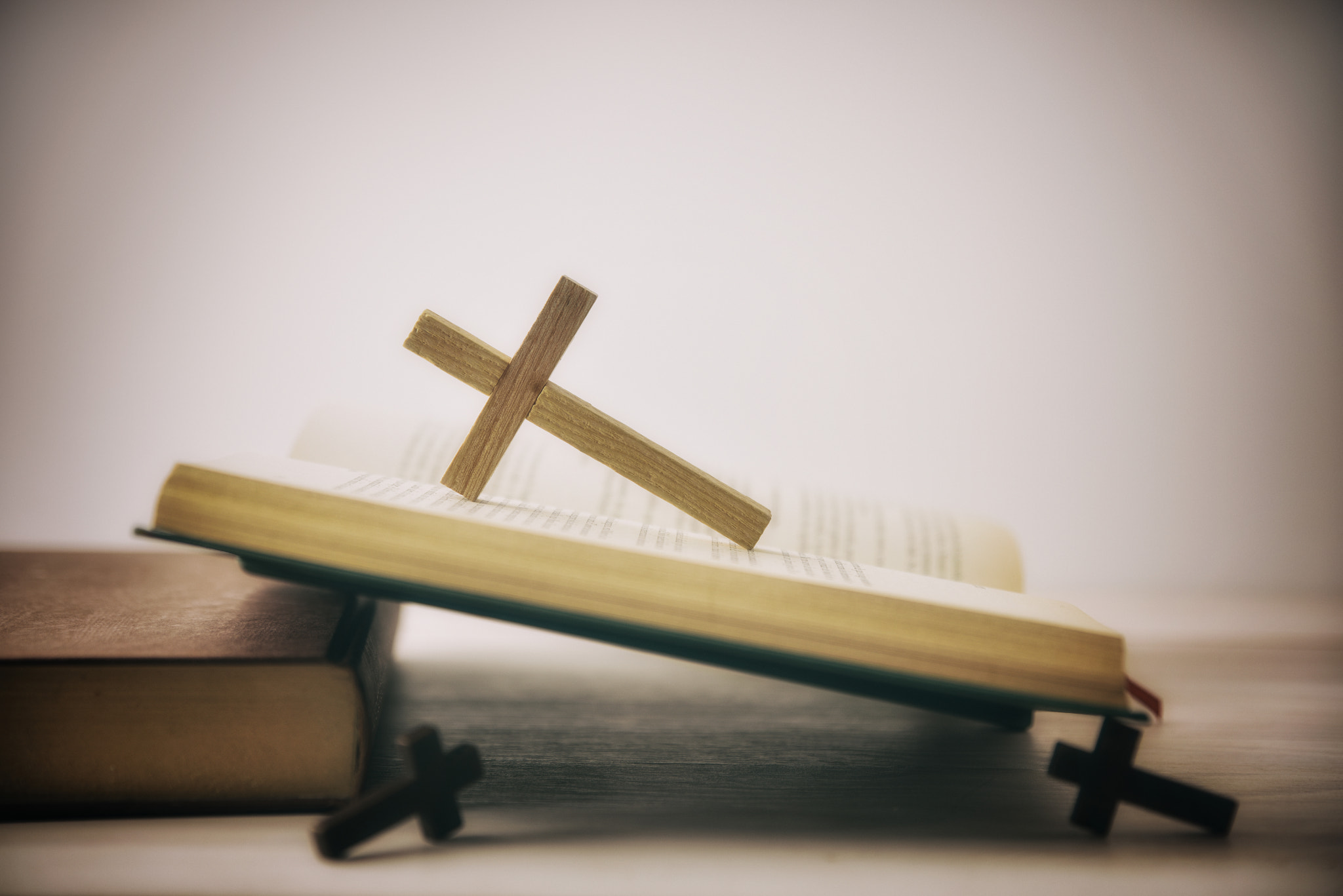 Old open Bible on wooden table with several wooden crosses