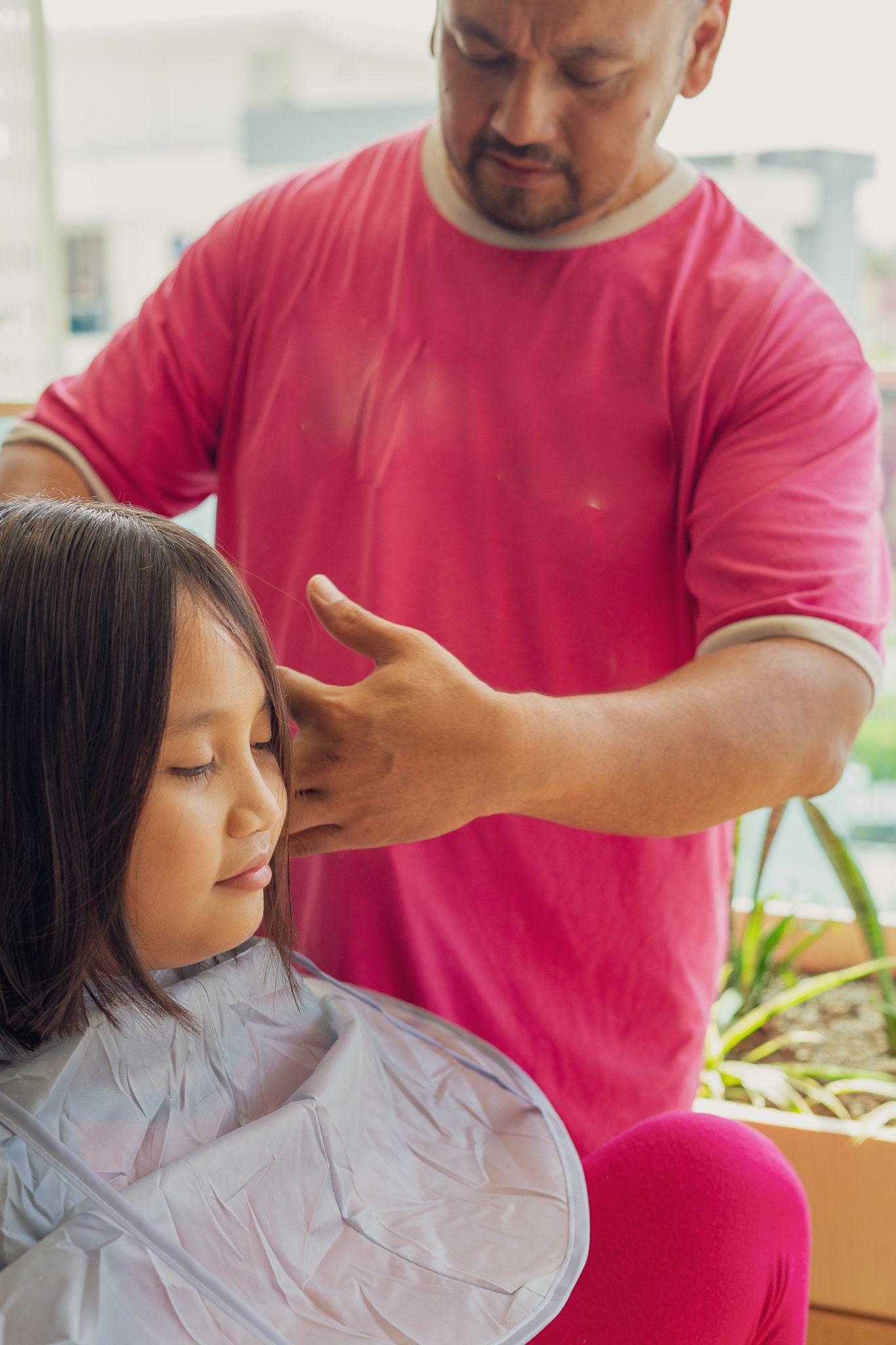 Asian young girl getting haircut at the apartment home balcony from the father