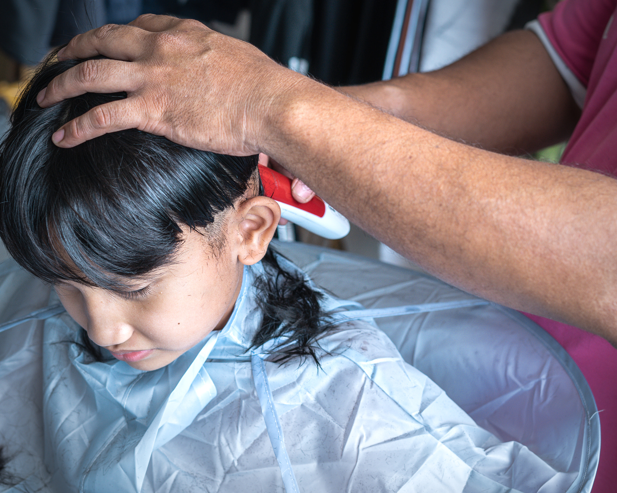 Asian child getting haircut at home from the father.