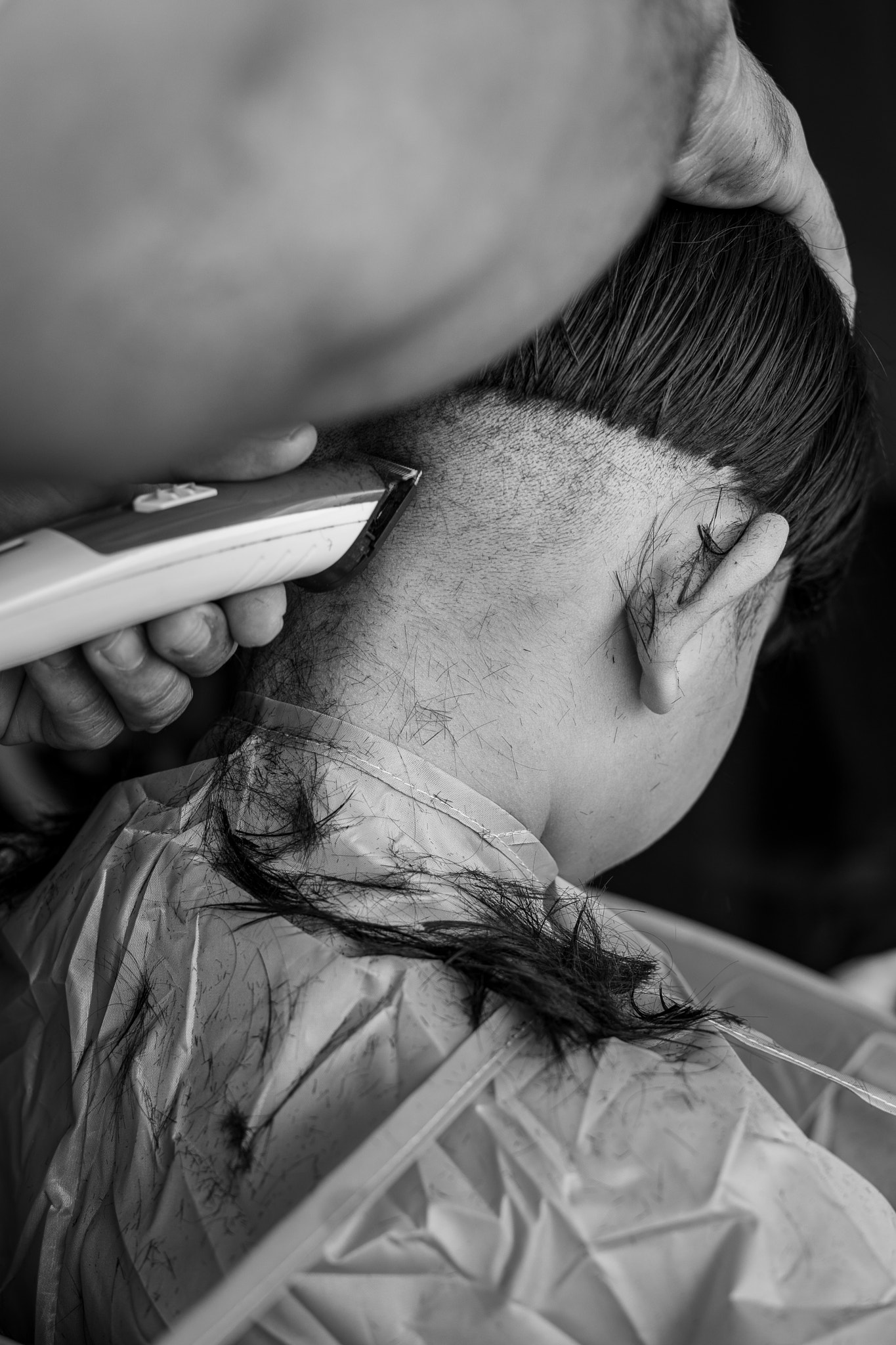Asian child getting haircut at home from the father. View from behind. Monochrome, black and white.