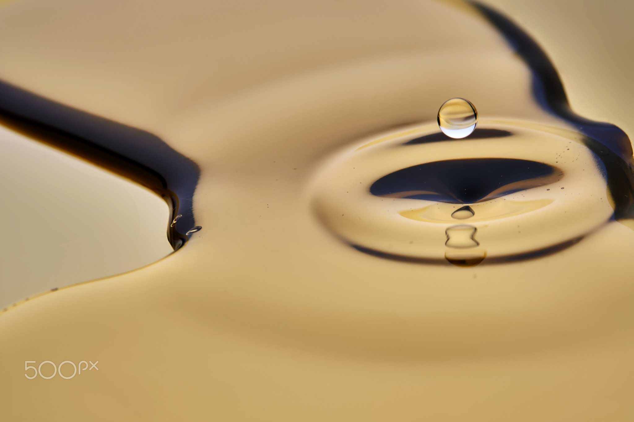 Texture of cosmetic oil with falling drop on golden background.