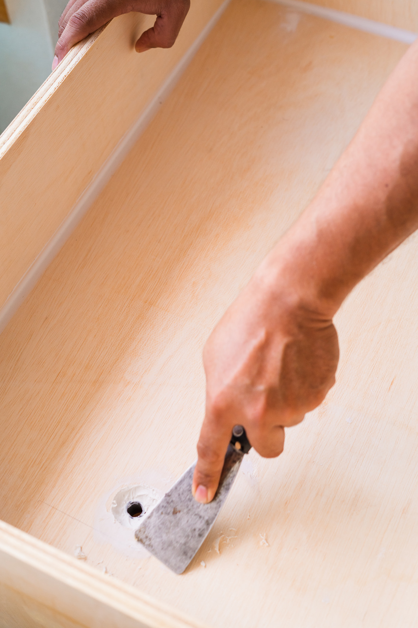Wooden surface and hand using scraper tool with white paint scraped.