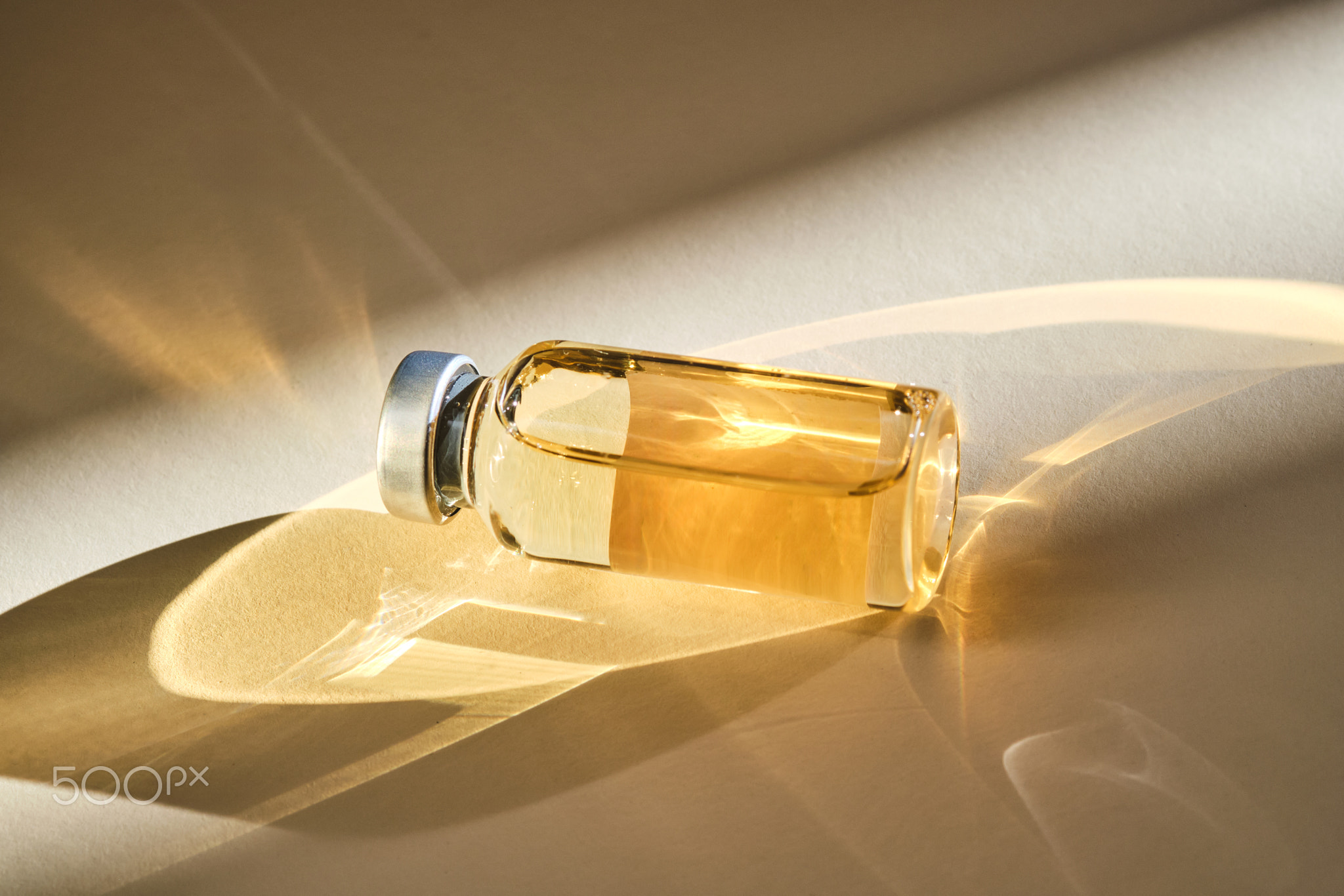 Injection vial with medicinal product in sunlight on beige background.